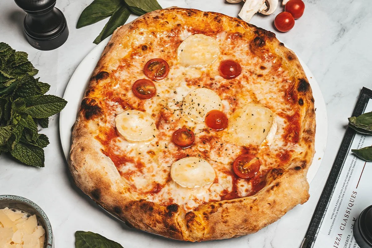 Une pizza aux tomates cerises, mozzarella et herbes sur une table en marbre.