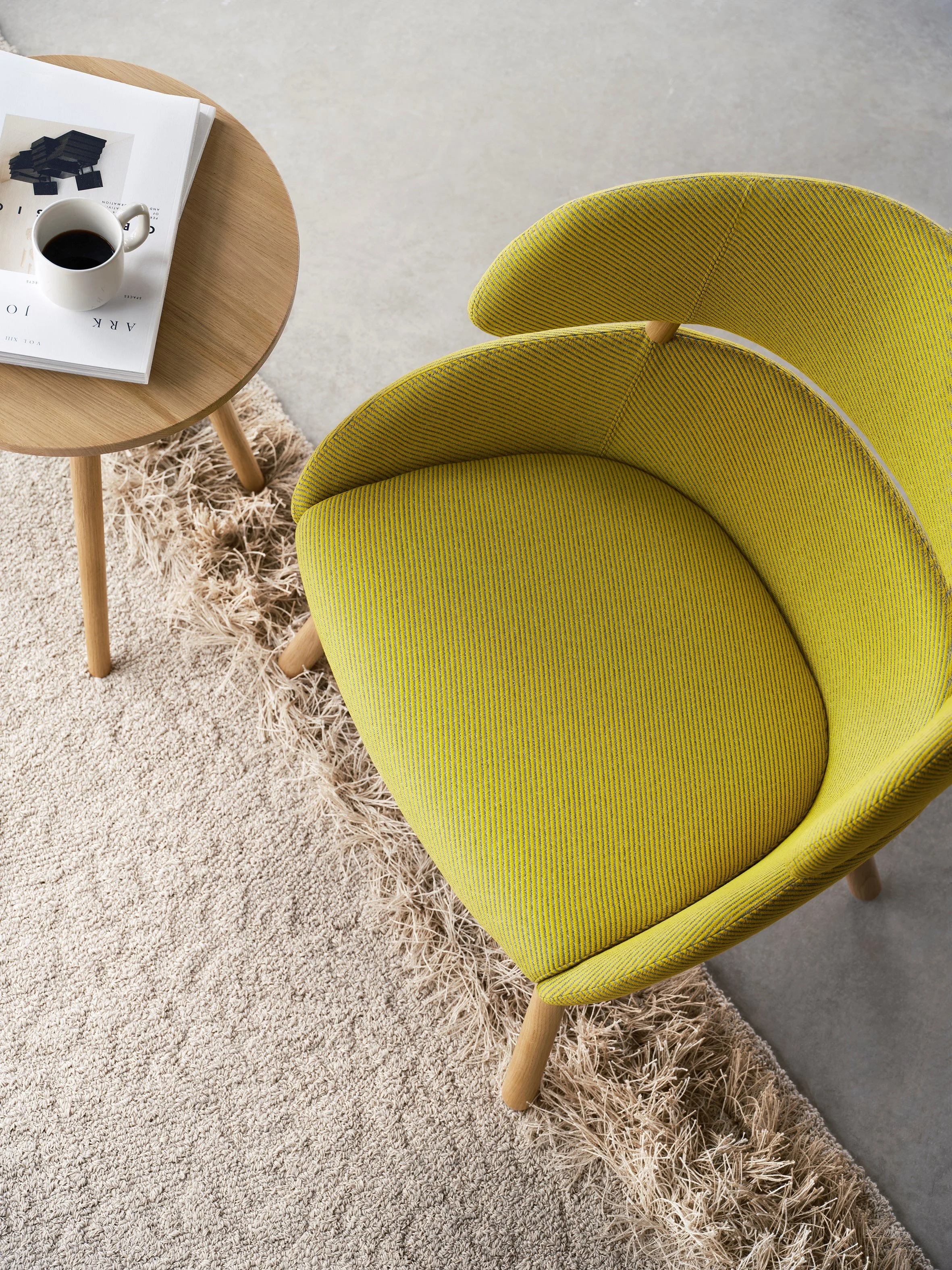 Et grønt lenestol, en rund bord med en kopp kaffe og magasiner på.