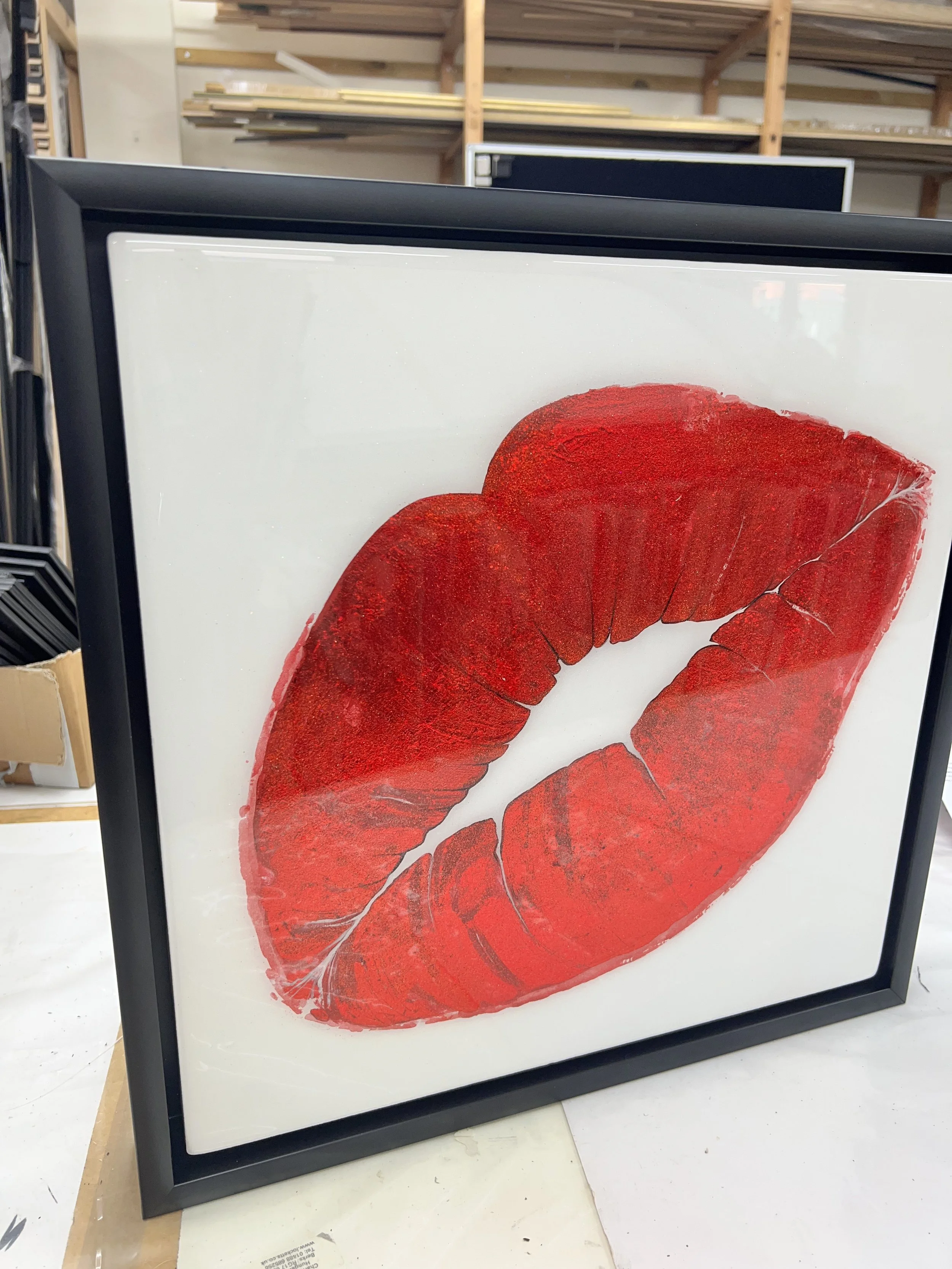 Framed artwork of red lips with detailed teeth, displayed in a workshop or art studio.