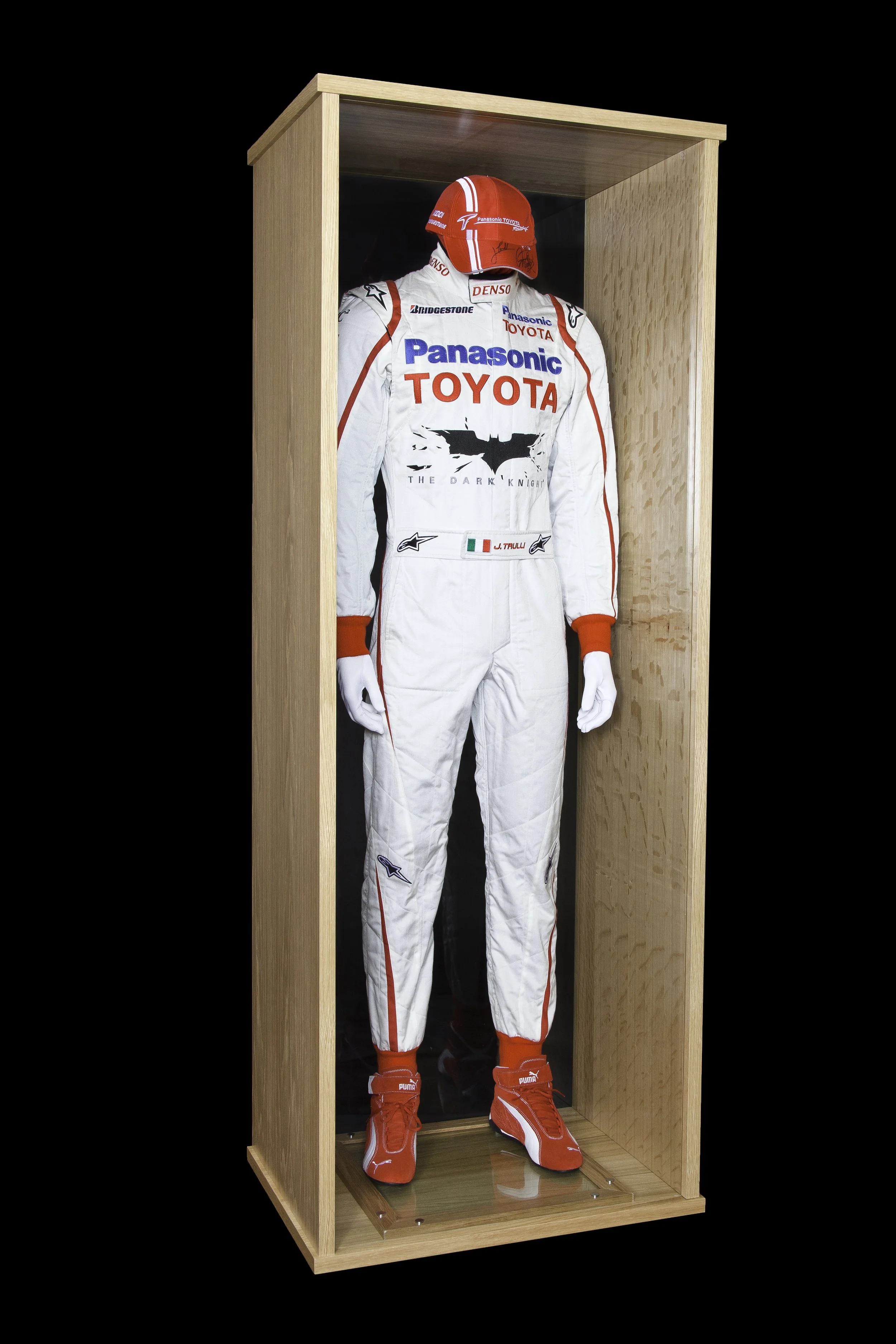 A racing driver's outfit and helmet displayed in a wooden glass case.