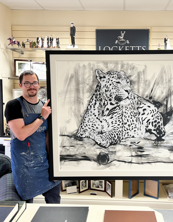 Man in black shirt and apron pointing at a large black-and-white drawing of a leopard in an art store.