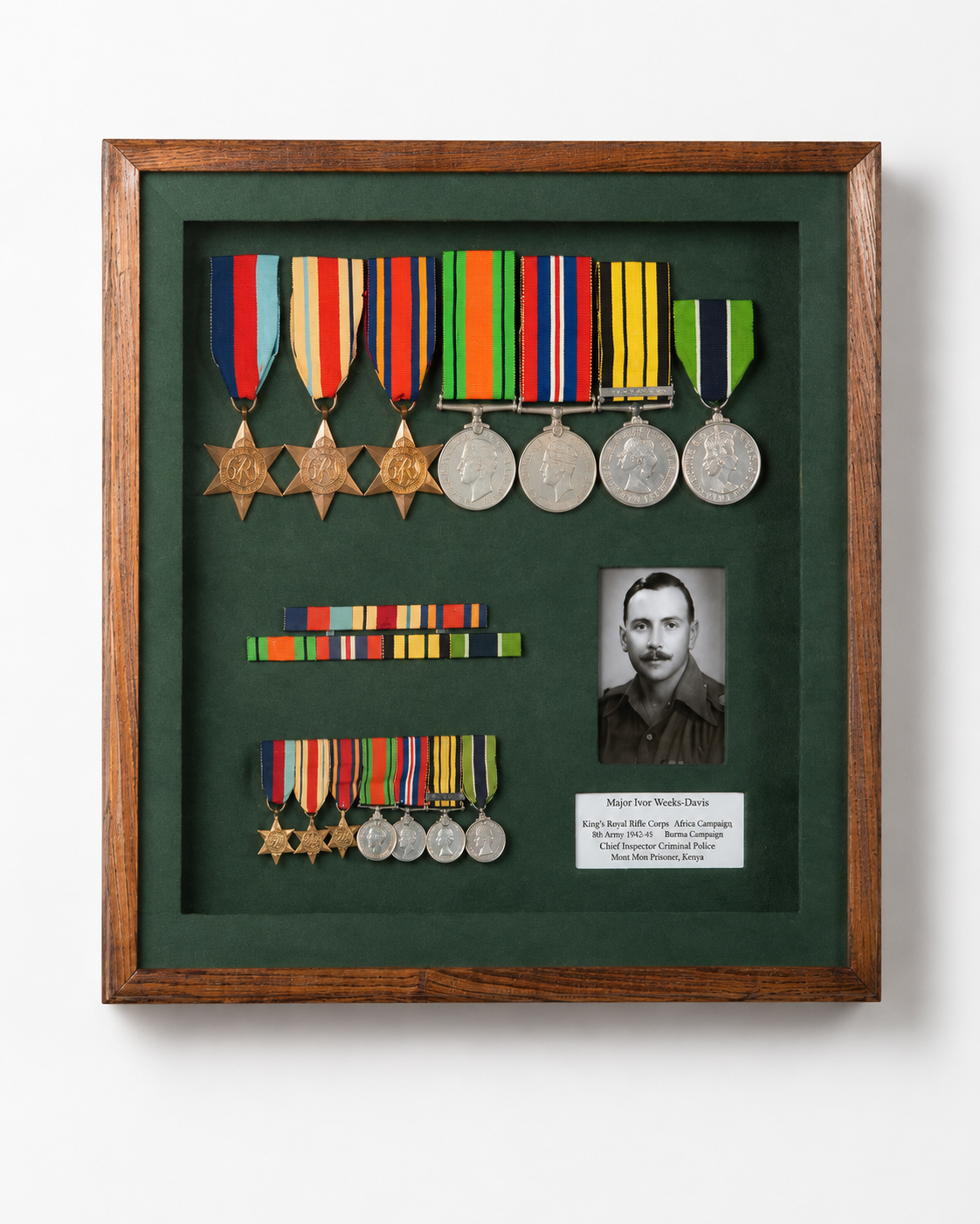 Framed display of military medals, a black and white portrait of a man, and a nameplate. The medals include gold and silver medals with colorful ribbons, arranged on a green background within a wooden frame.
