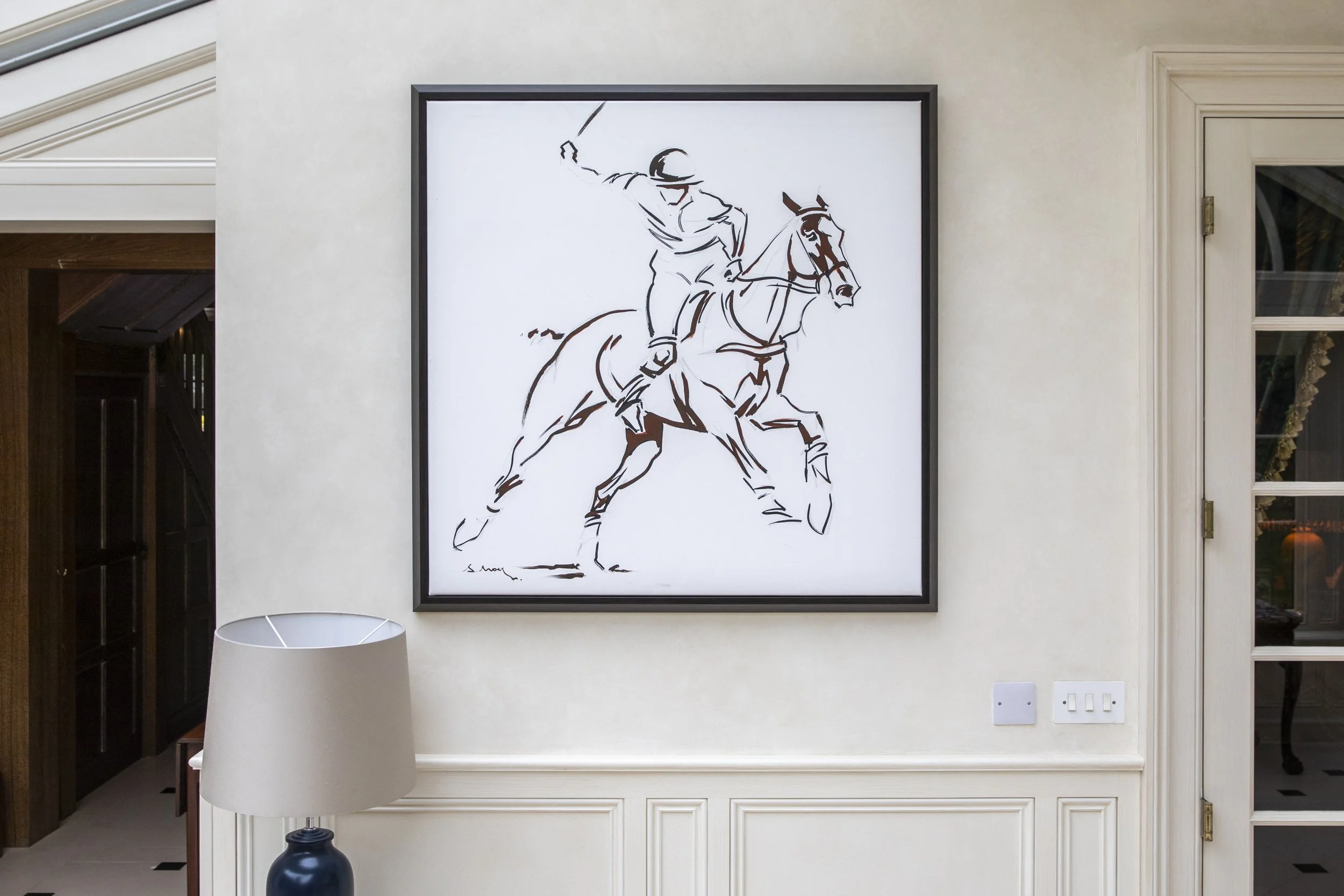 Minimalist artwork of a polo player on a horse, drawn with black lines on a white background, framed and hanging on a wall in a modern interior.