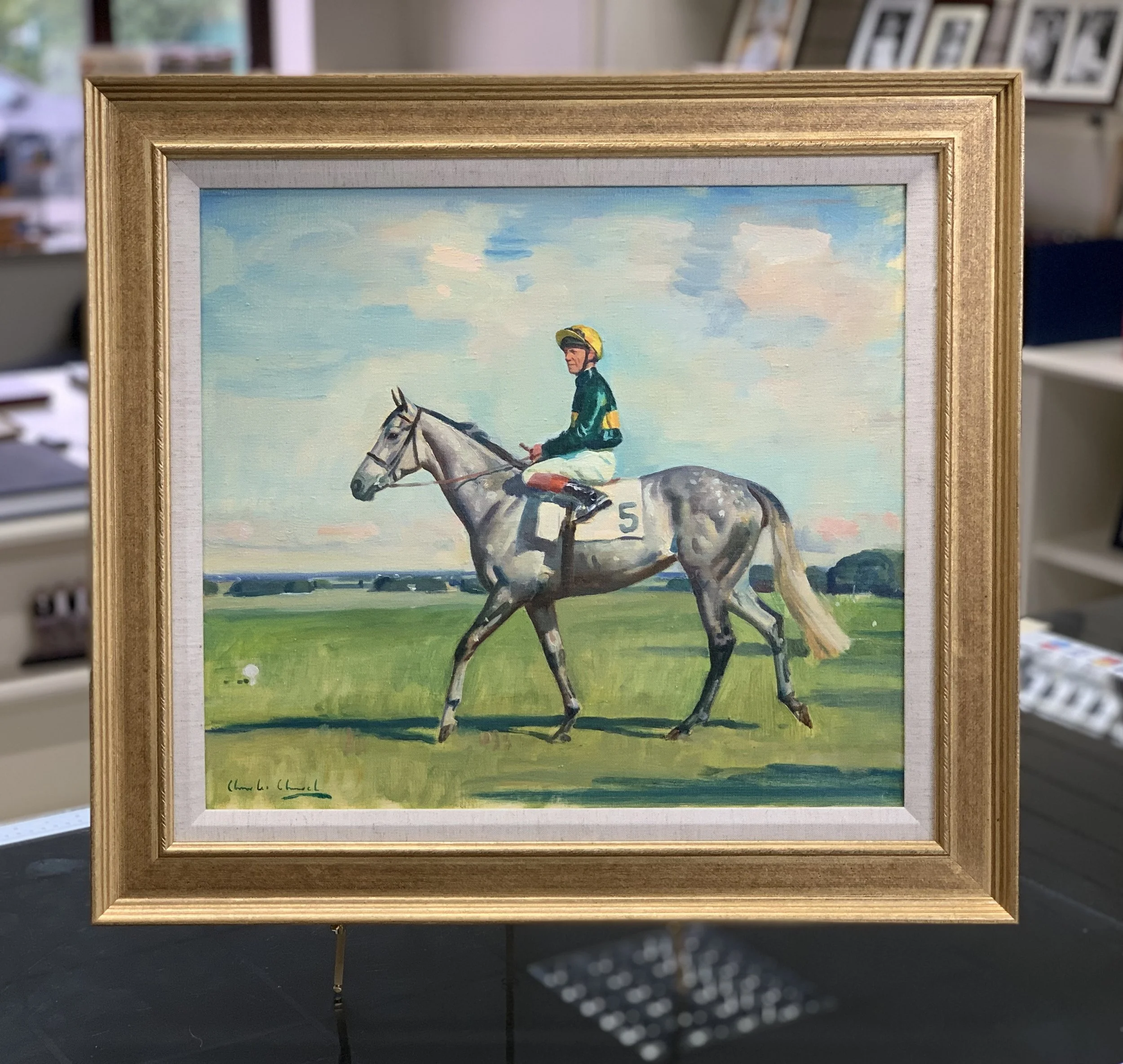 Framed watercolor painting of a jockey riding a gray horse against a light blue sky with clouds.