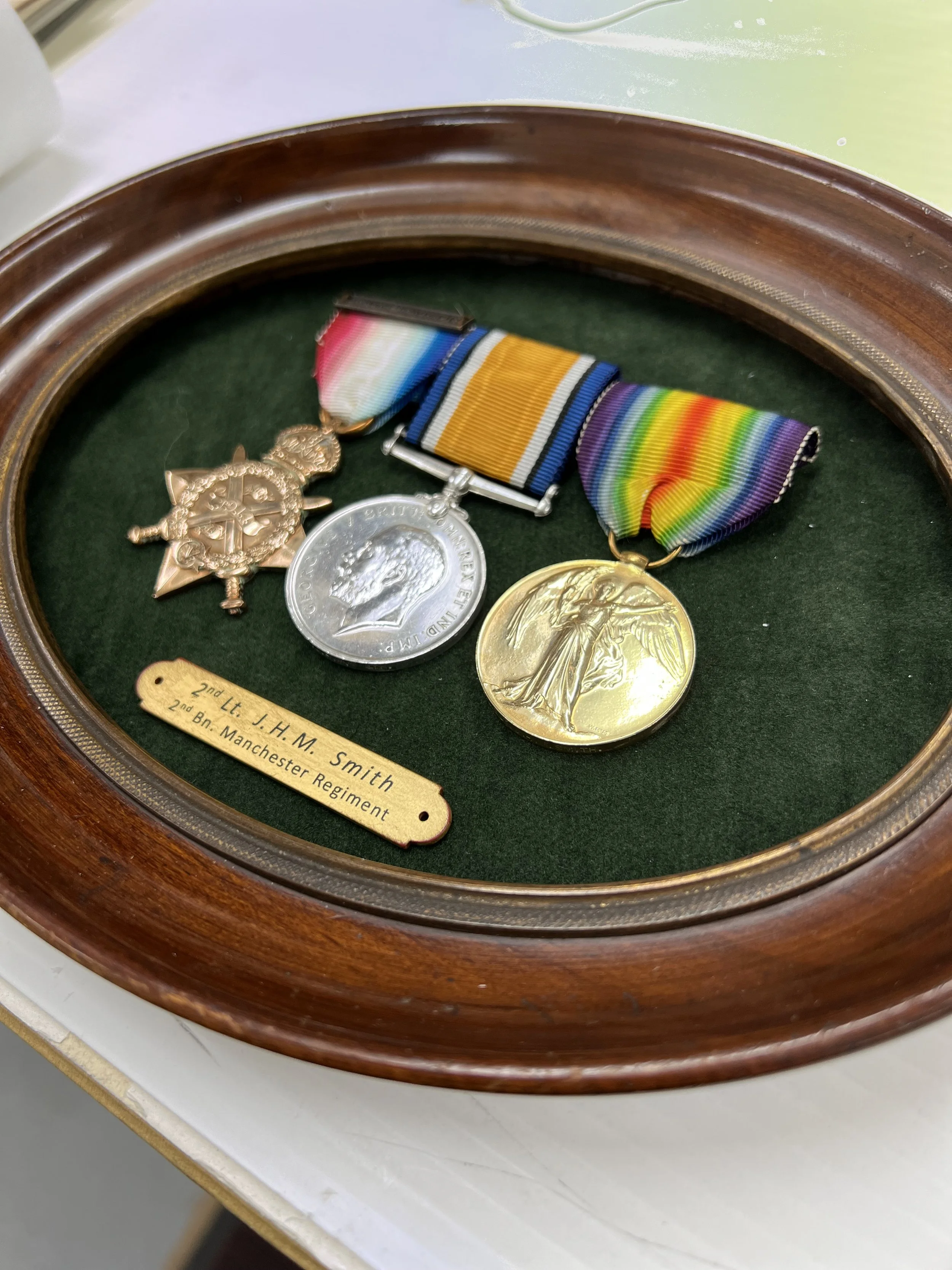 Medals displayed in a wooden and glass display case, with a green velvet background. The medals include a gold, silver, and bronze medal with ribbons, and a metal badge with a ribbon, along with a small brass plaque indicating they belong to 2nd Lt. 