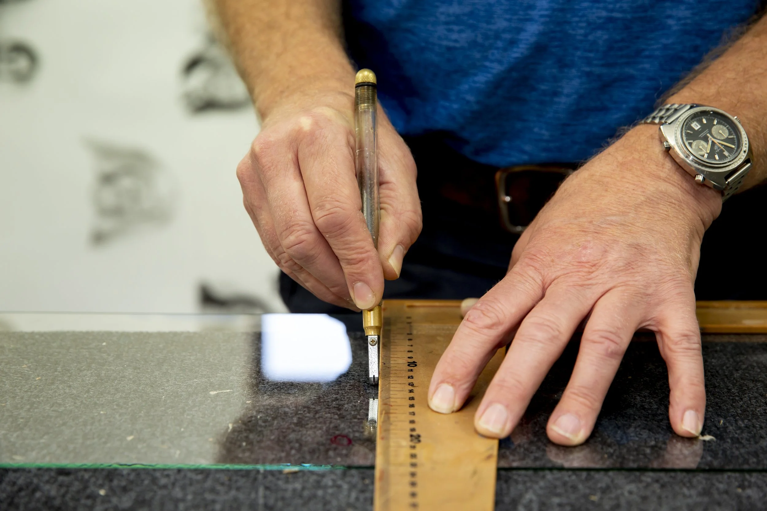 Person using a handsaw to cut a wooden ruler on a black work surface, wearing a silver wristwatch.