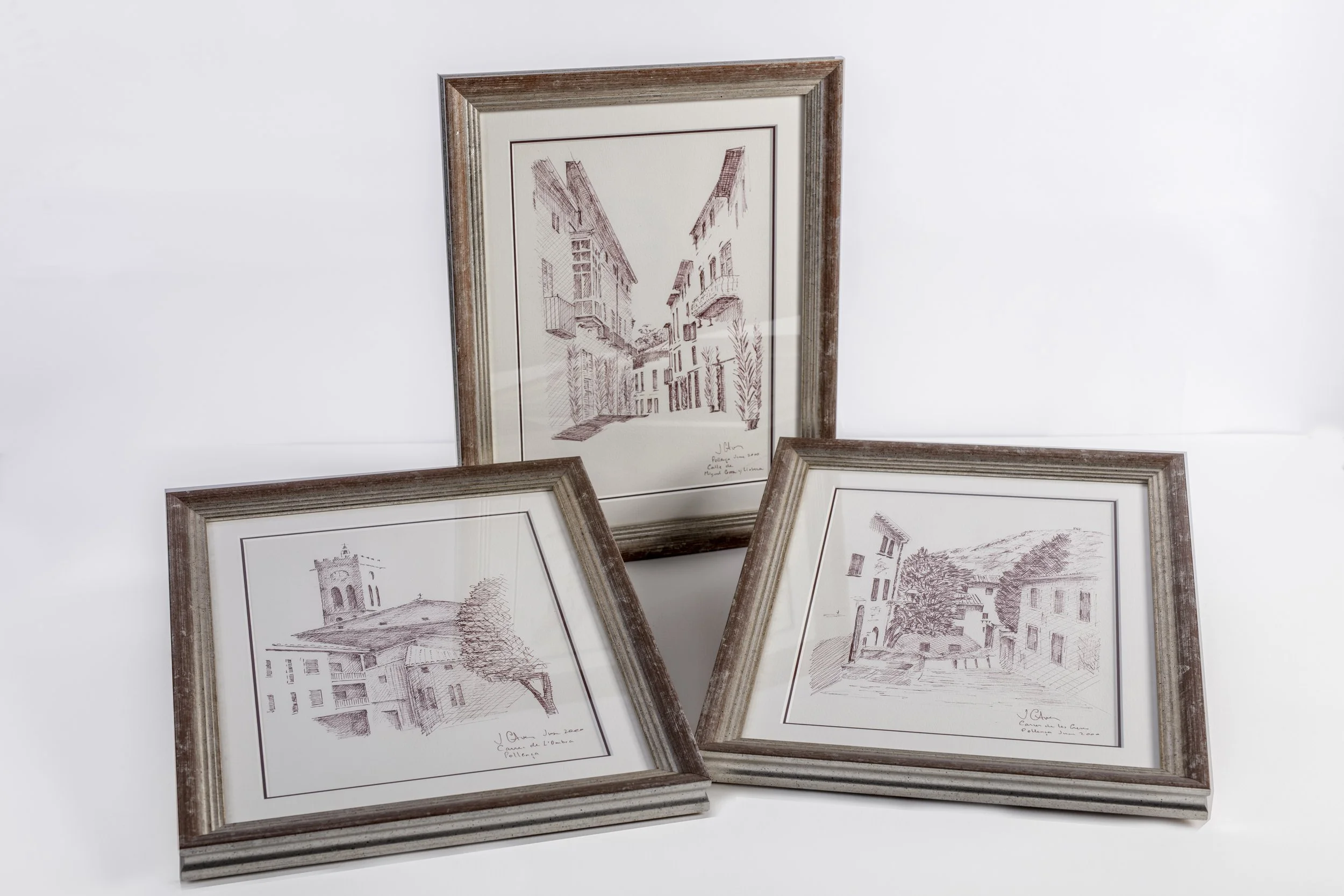 Four framed architectural sketches of buildings and streets, with two leaning against a white wall and two lying flat.