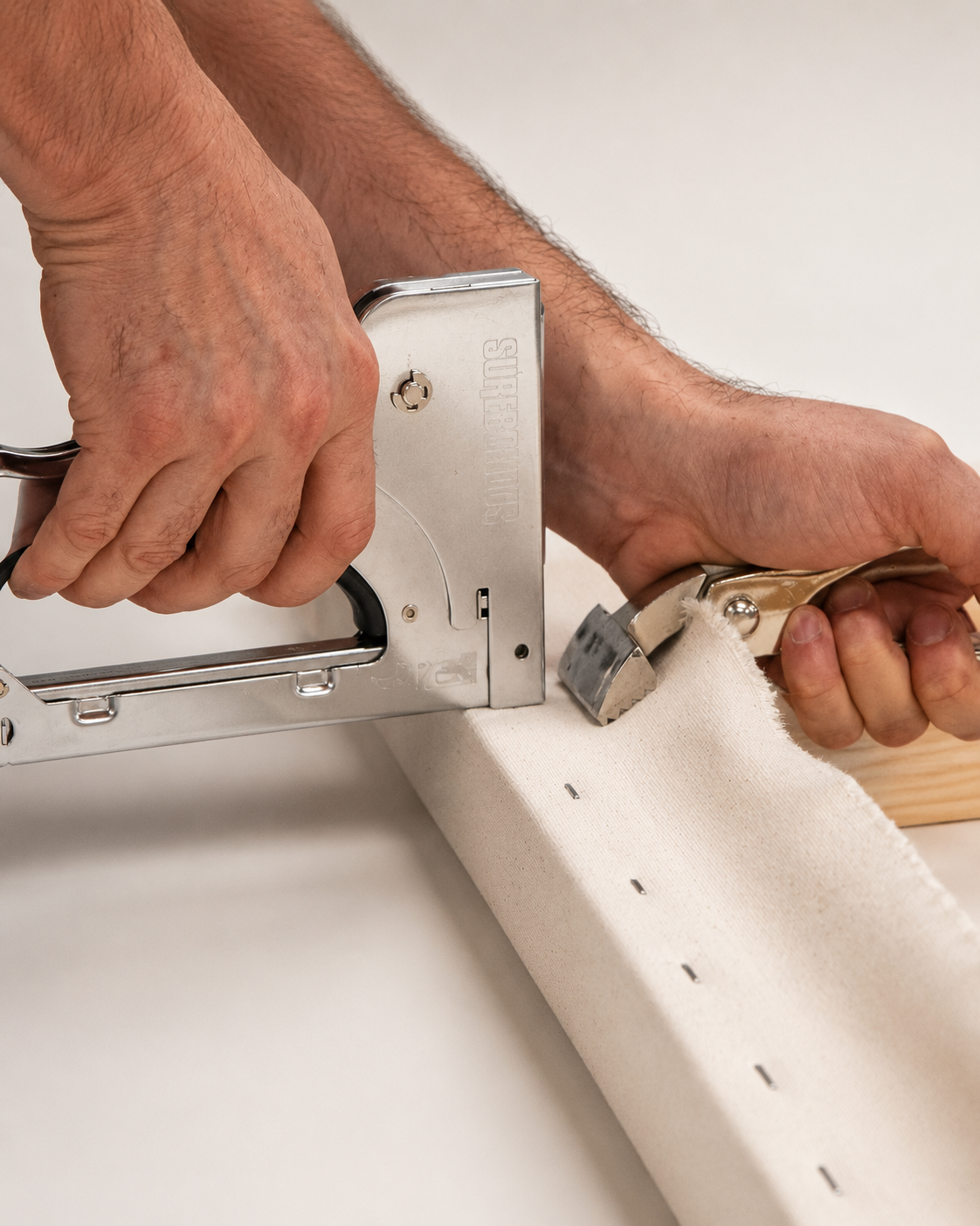 Person using staple gun to fasten fabric to wooden frame.