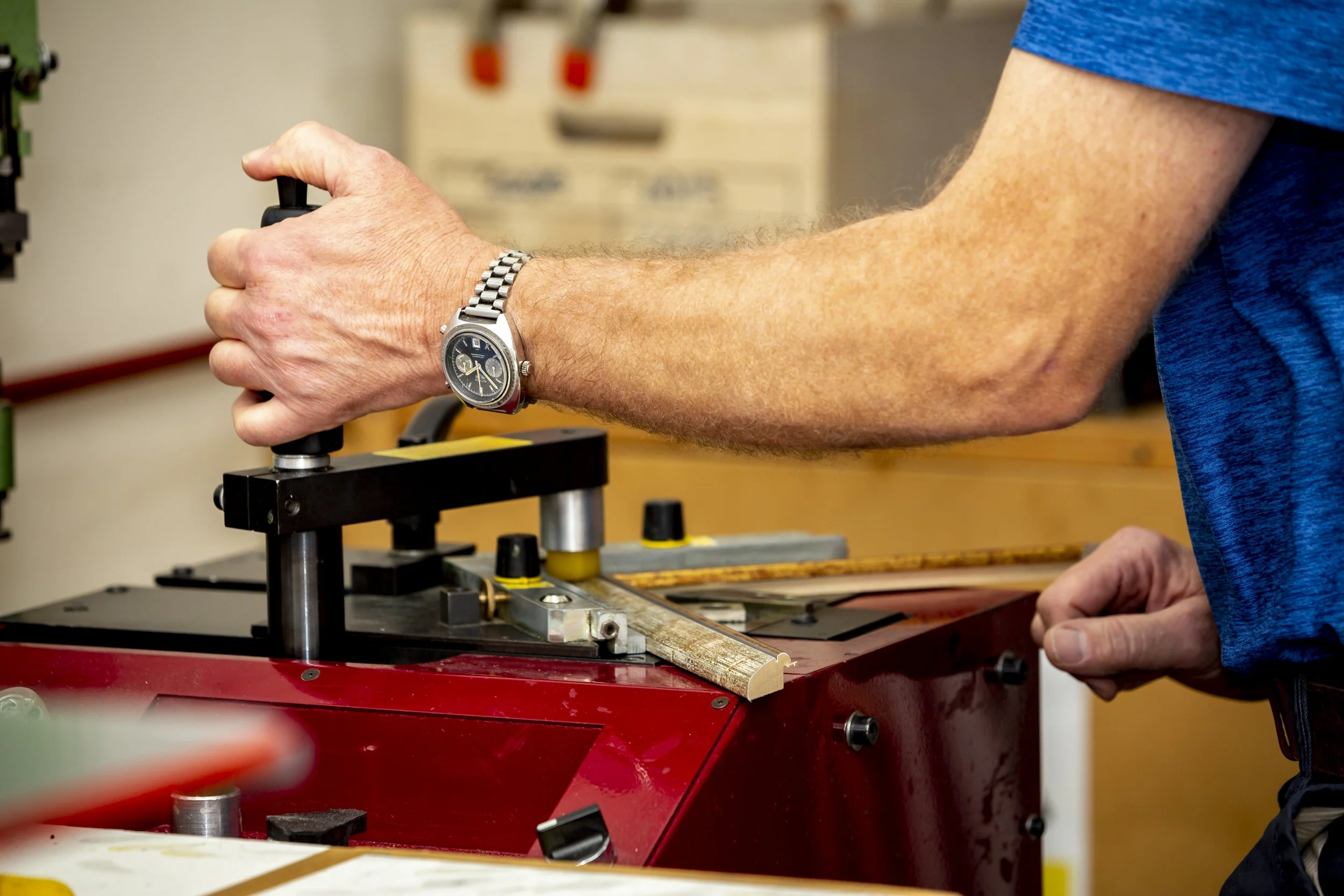 A person wearing a blue shirt and a wristwatch is operating a machine with their hands in a workshop or lab setting.