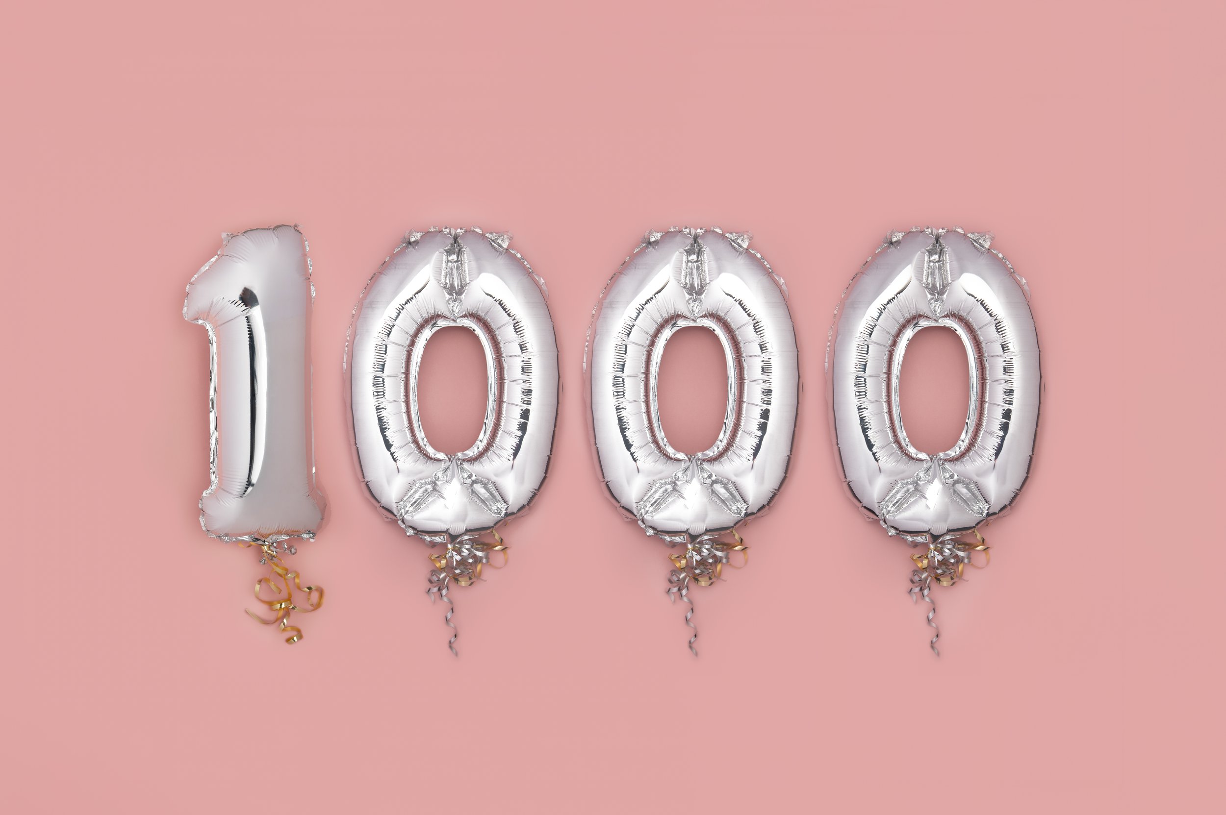 Silver number and letter balloons spelling out "1000" on a pink background.