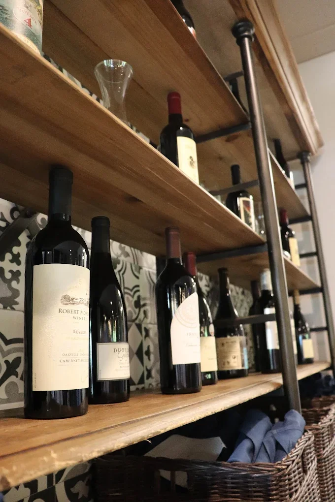 Wooden wine rack with bottles of red wine, a glass decanter on top shelf, and a basket filled with cloth below.