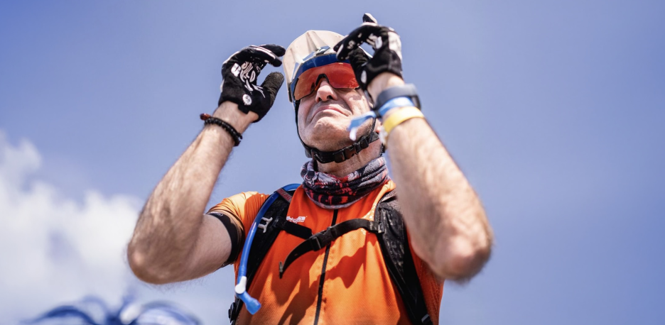 Un hombre en equipo de protección ajustándose un casco y gafas de sol en un día soleado de montaña.