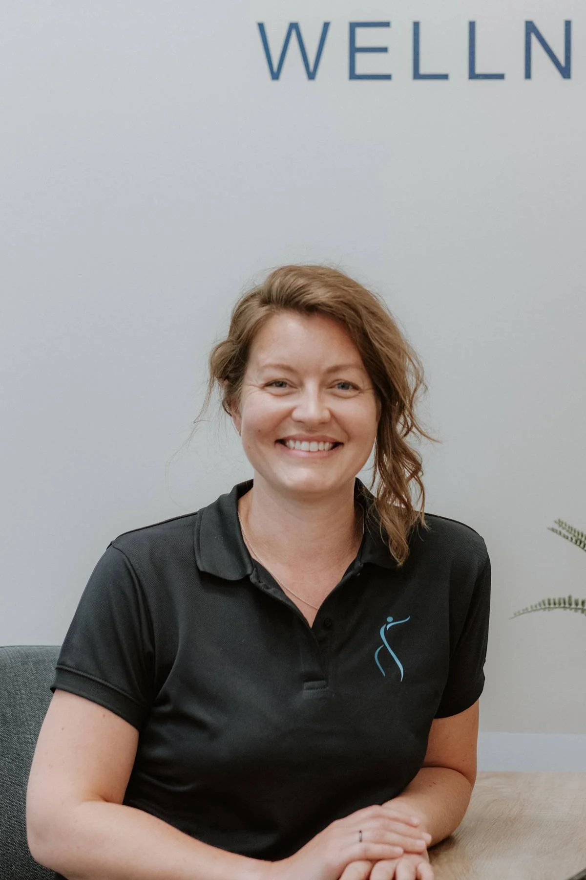 Laura Rutterford, Chartered Physiotherapist at Quay Kinetics Physio, seated at a desk with a plant and window in the background