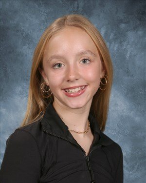 A young woman with red hair styled in an updo, sitting outdoors at night, with snow on the ground and city lights in the background.