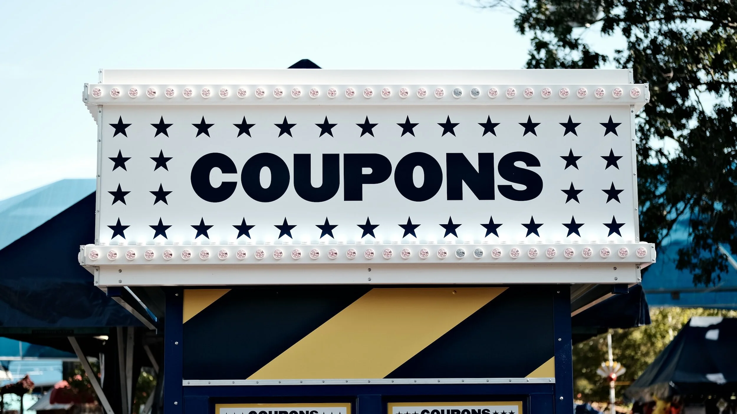 A sign with the word 'COUPONS' in large bold letters, decorated with black stars and surrounded by light bulbs, likely at a carnival or fair.