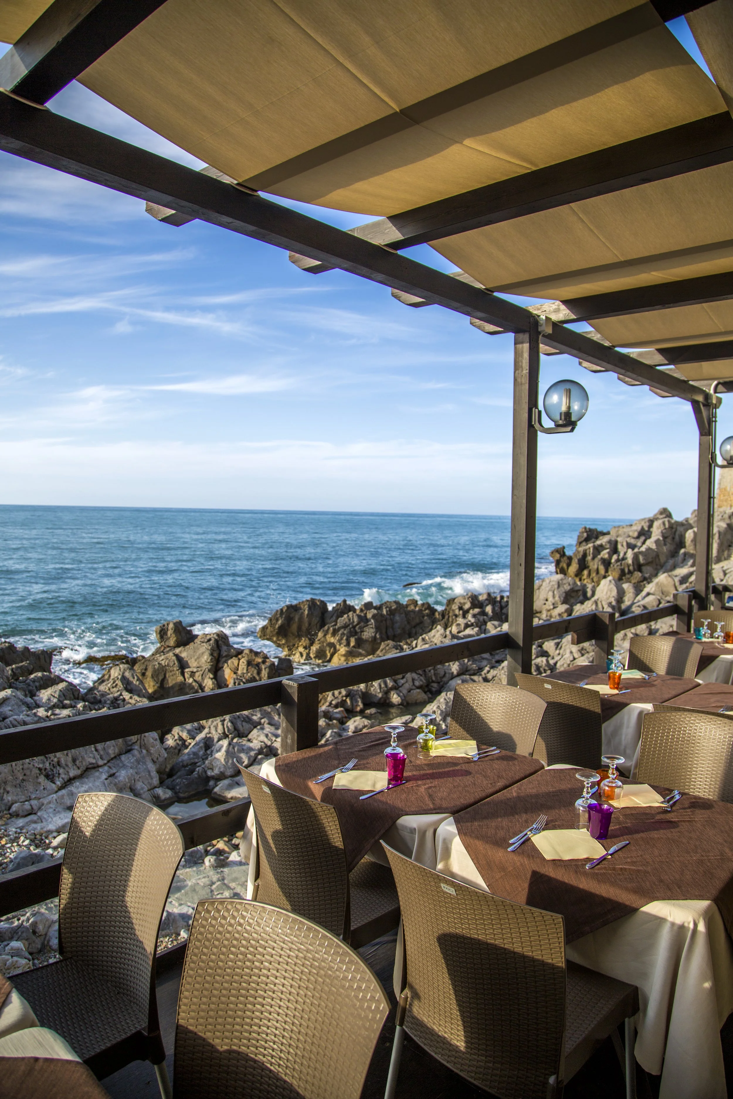 Restaurant im Freien mit Tischen und Stühlen und Blick auf den Atlantik, mit felsiger Küste und blauem Himmel.