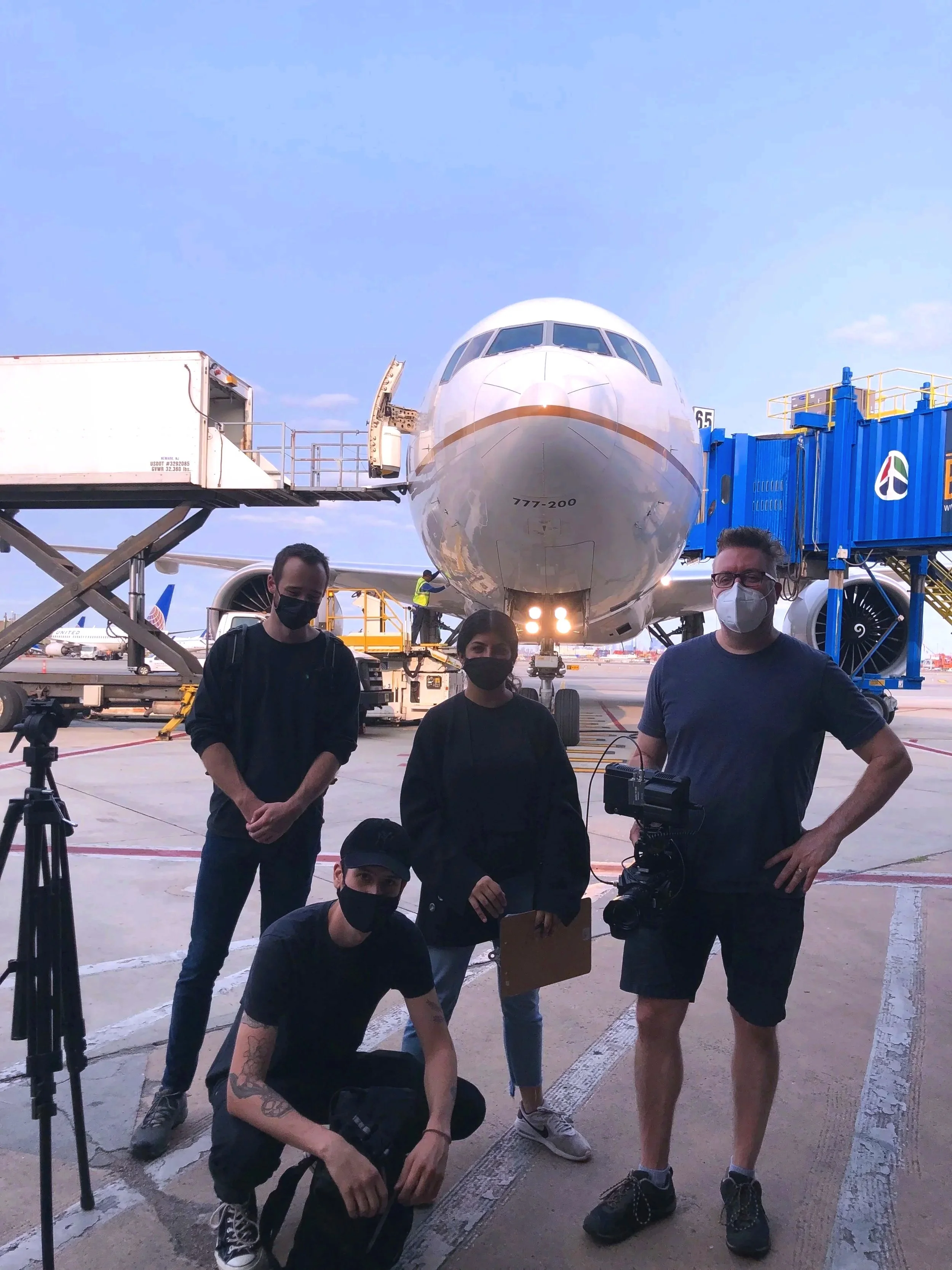 Ein Filmteam steht auf dem Rollfeld vor einem Flugzeug, das an einem Flugsteig geparkt ist. 