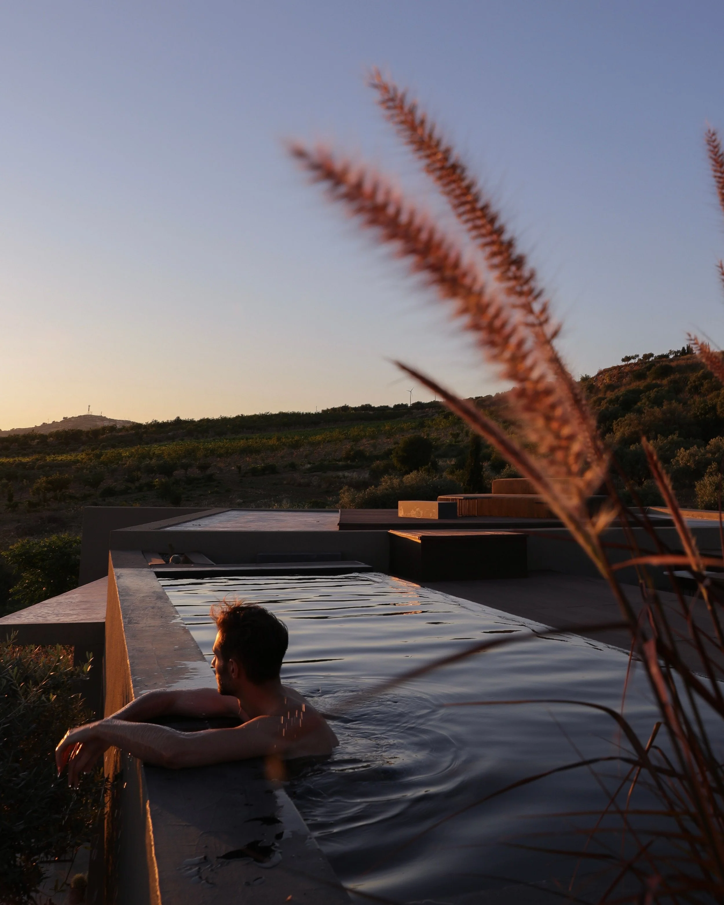 A tranquil outdoor swimming pool surrounded by lush greenery, trees, and rocks, with a rocky hillside in the background as private, Portuguese accommodation.