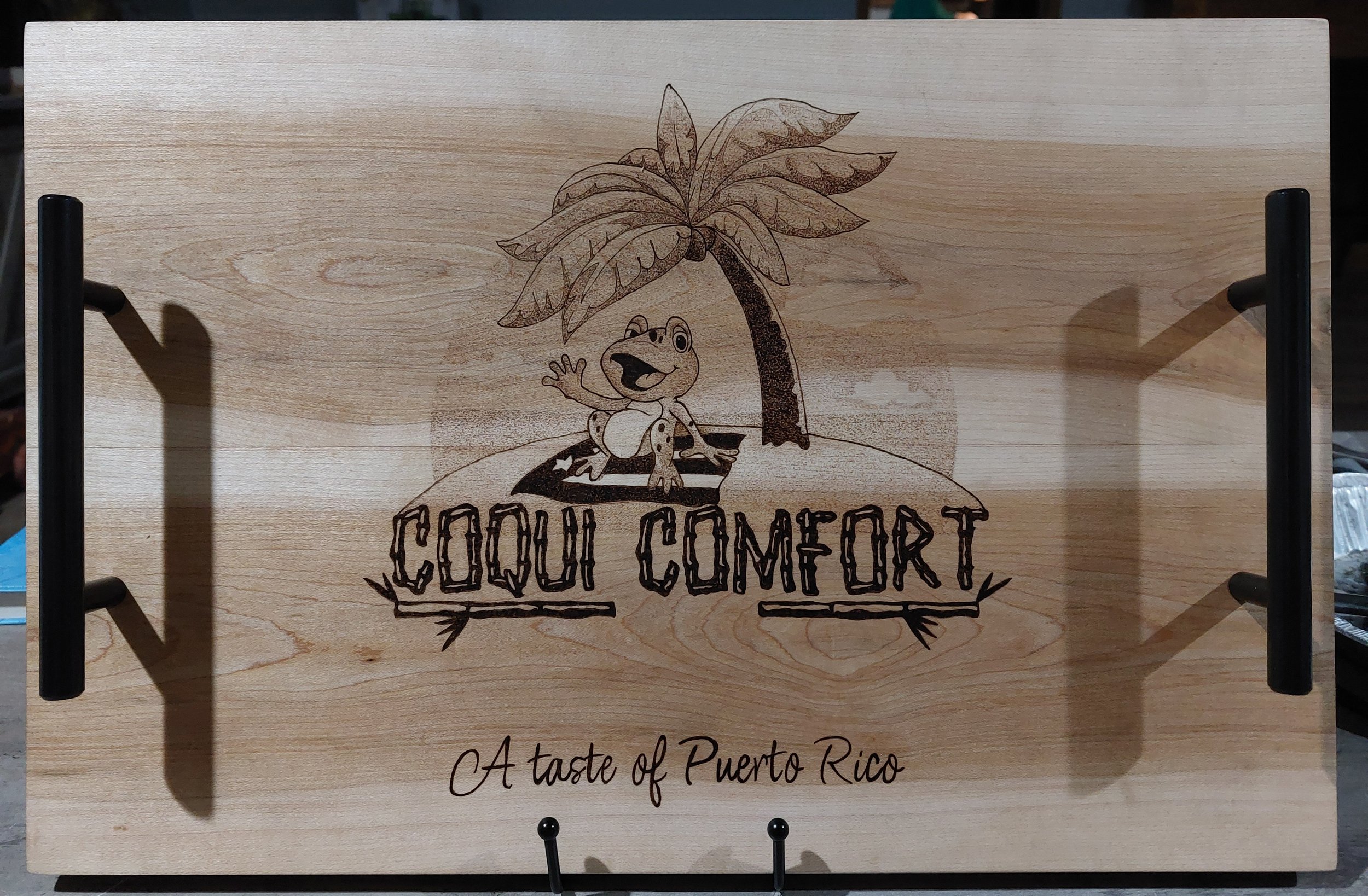 Wooden serving tray with handles that has a cartoon frog under a palm tree and the words "Cocui Comfort" with a tagline "A taste of Puerto Rico."