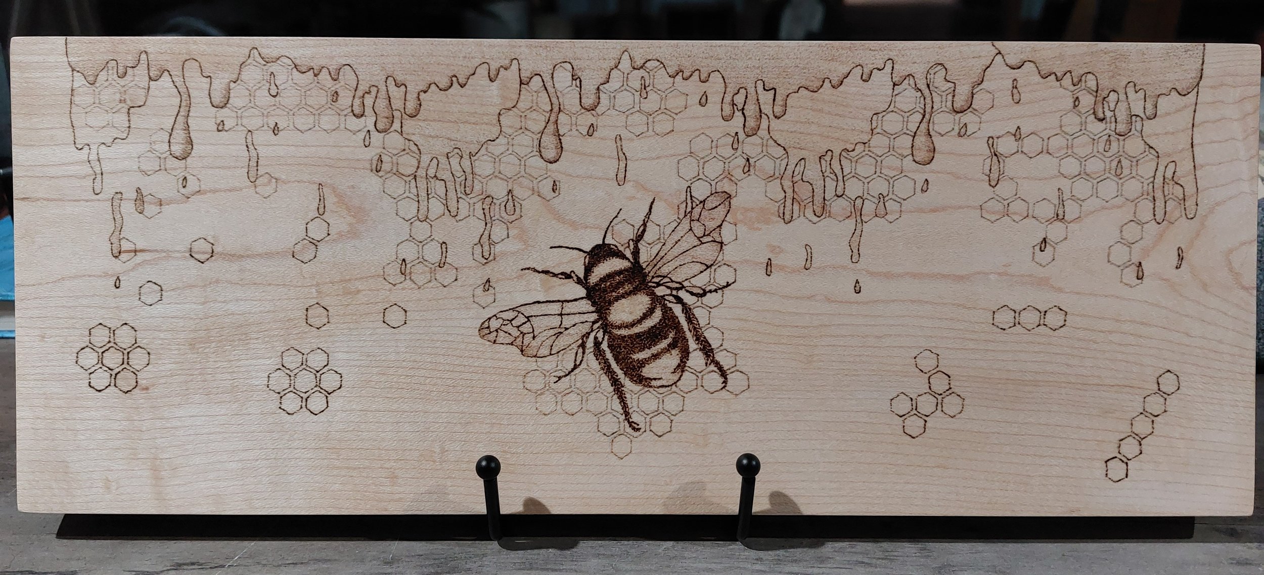 Wooden plaque with a hand burned design of a honeybee and honeycomb pattern.