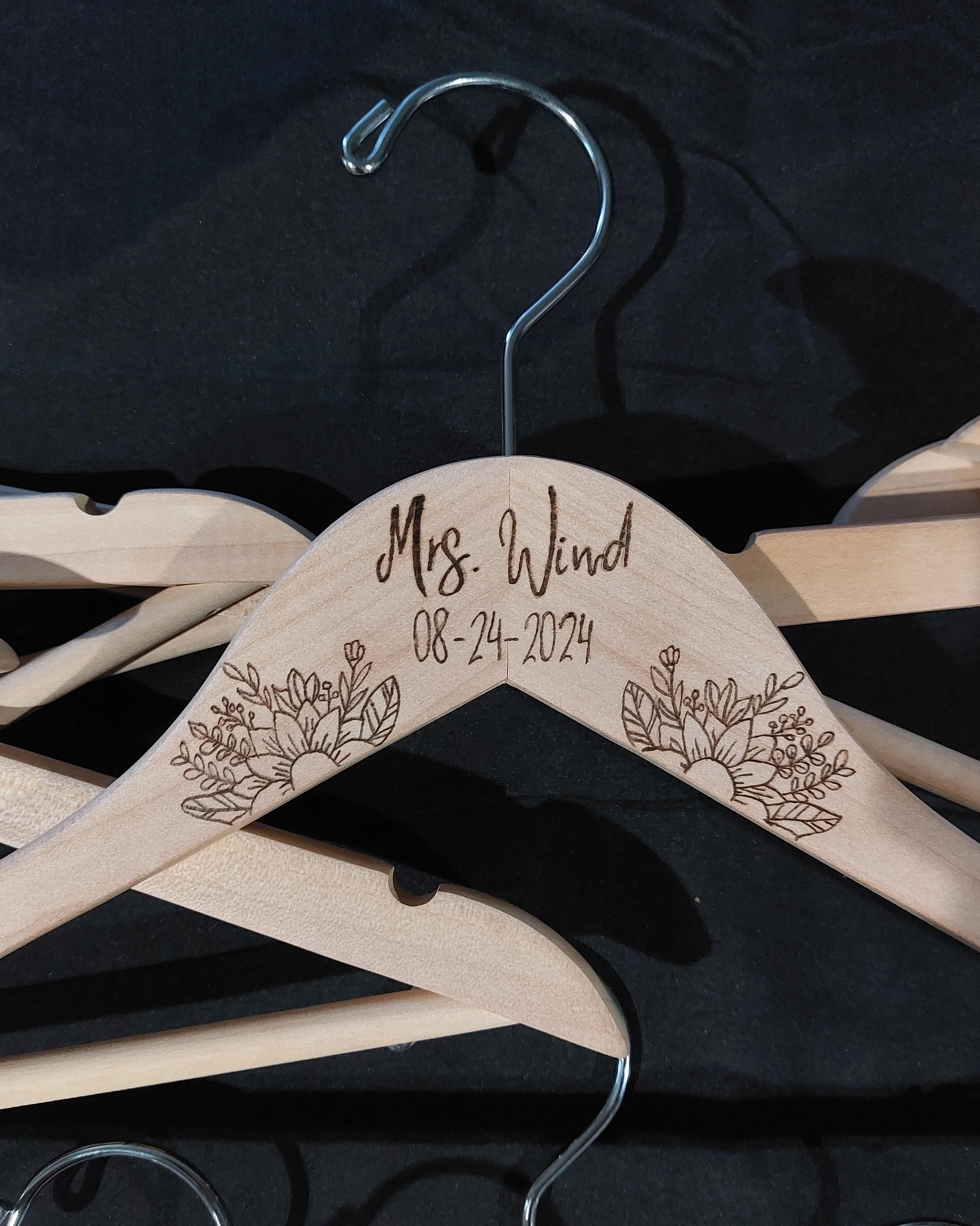 Wooden hanger hand burned with the name 'Ms. Wind' and the date '08-24-2024', featuring hand burned floral designs on each side.