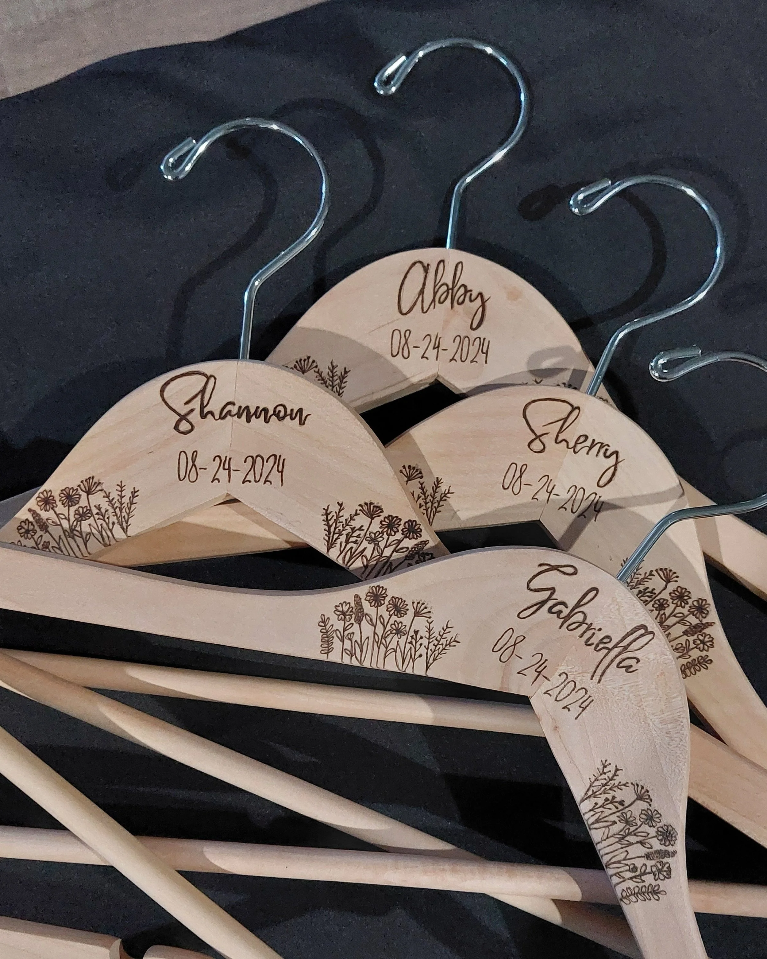 Wooden hangers hand burned with names and the date 08-24-2024, decorated with floral designs.