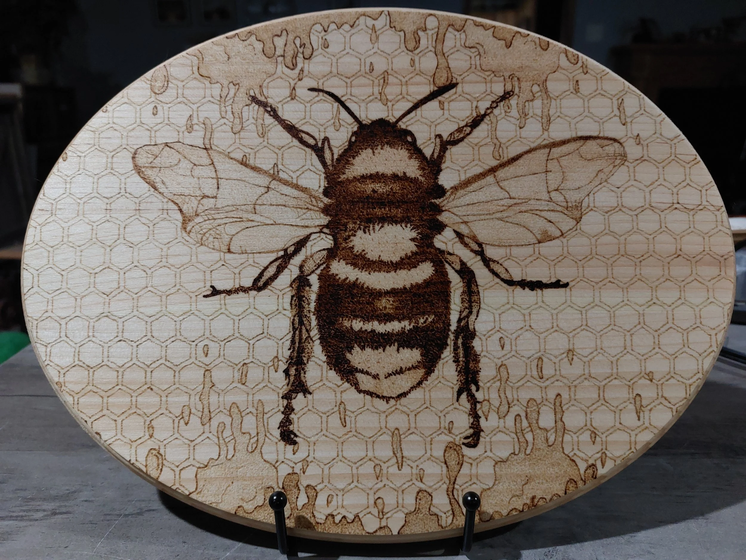 Wooden plaque with a stippled burned design of a bee and honeycomb pattern in the background.