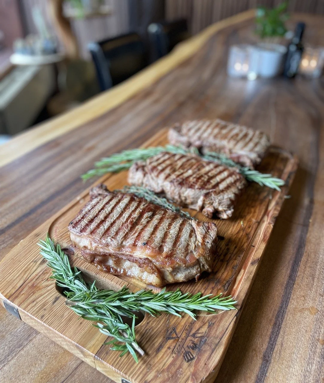 Gegrilde entrecôtes met takjes rozemarijn op een houten snijplank in een steakhouse.