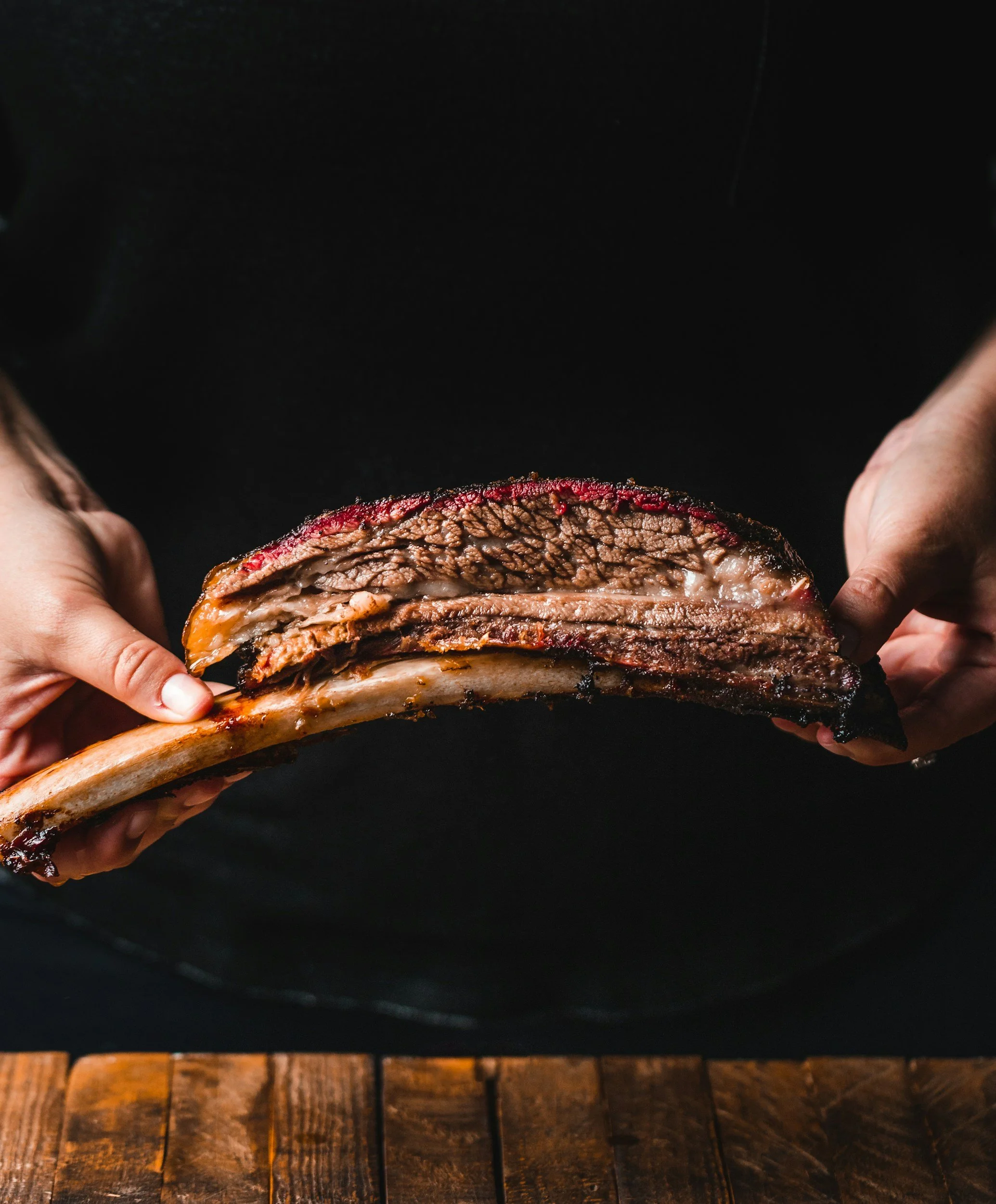 Persoon houdt een stuk geroosterde sparerib met vlees en bot in handen, klaar om te eten.