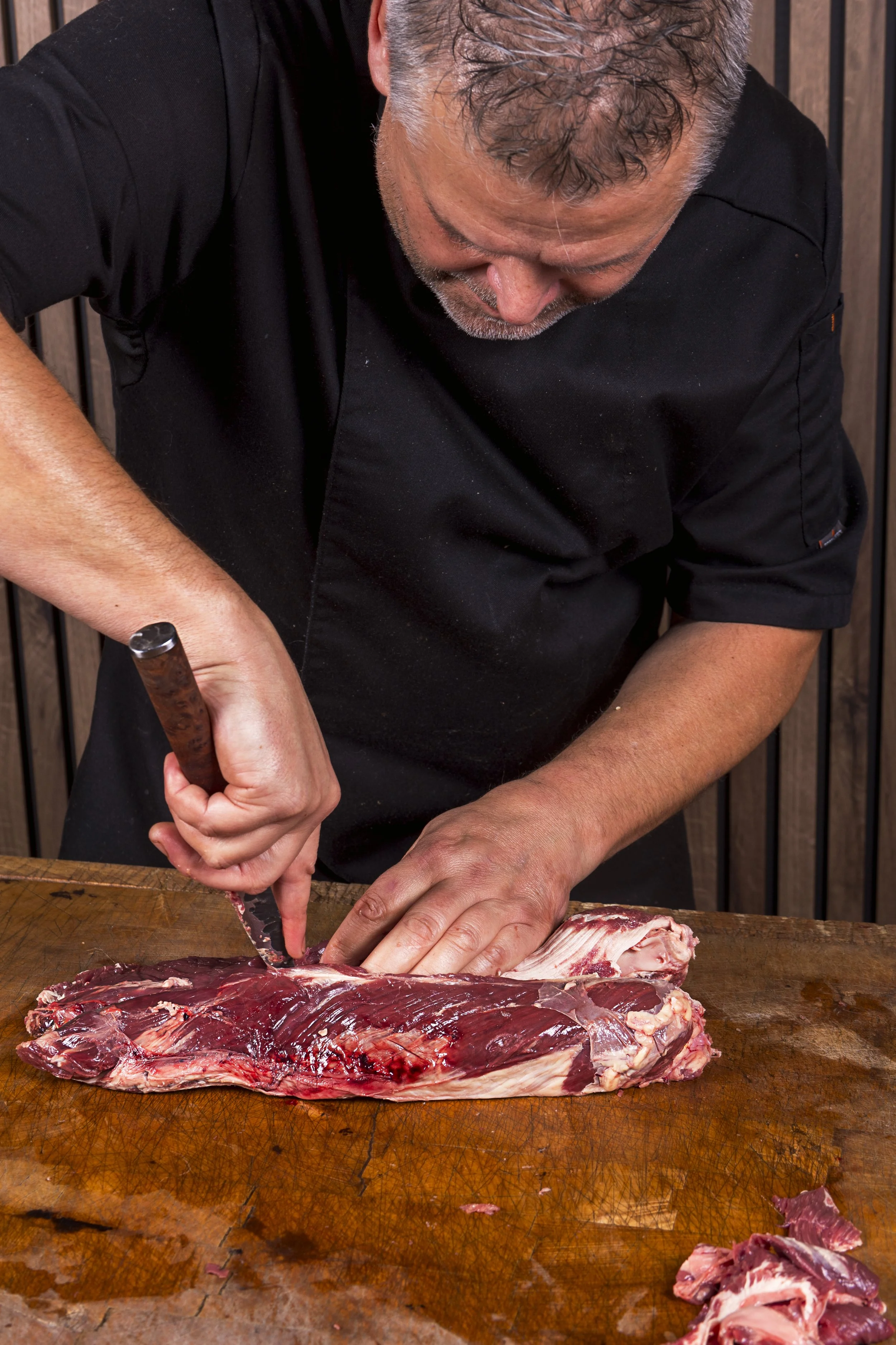 Man snijdt vlees met een mes op een houten snijplank.