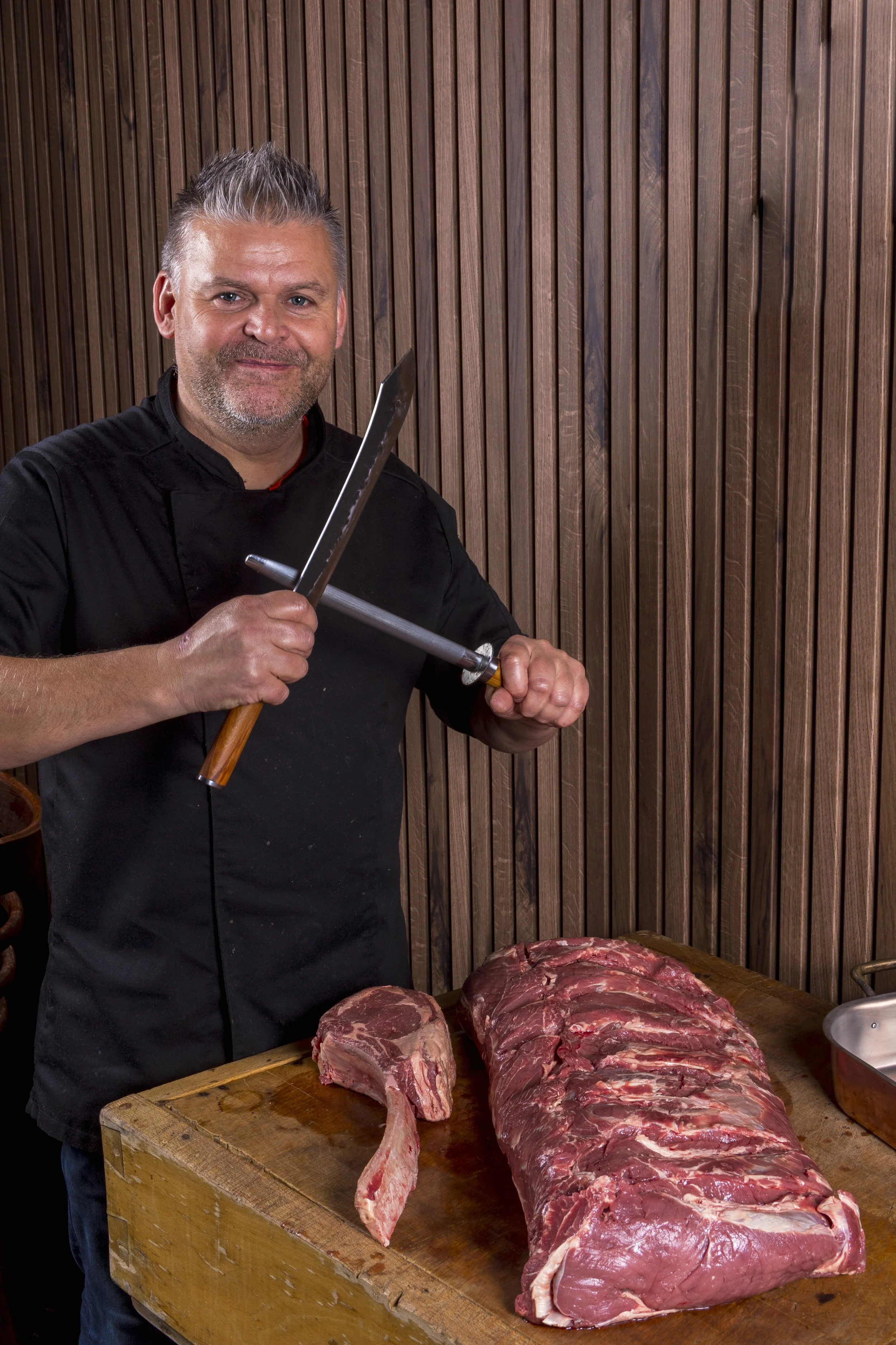Smakelijke man bereidt een stuk vlees voor op de snijplank in een restaurant met houten wand.
