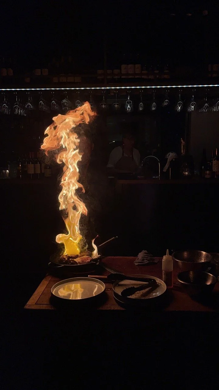 Vlammen die uit een kookpan komen tijdens het flamberen met een flambadou in een donker restaurant.