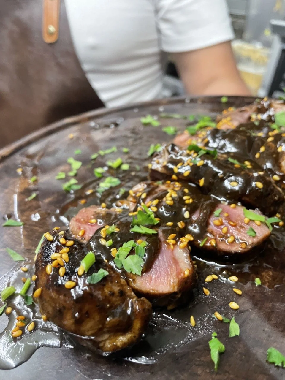 Gemarineerde eendenborst met sesamzaad en groene kruiden op een houten bord
