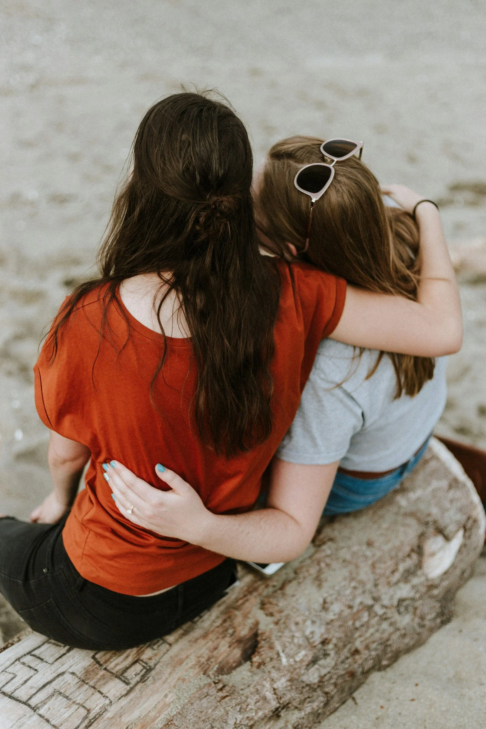 Two women are sitting on log giving a side  hug.