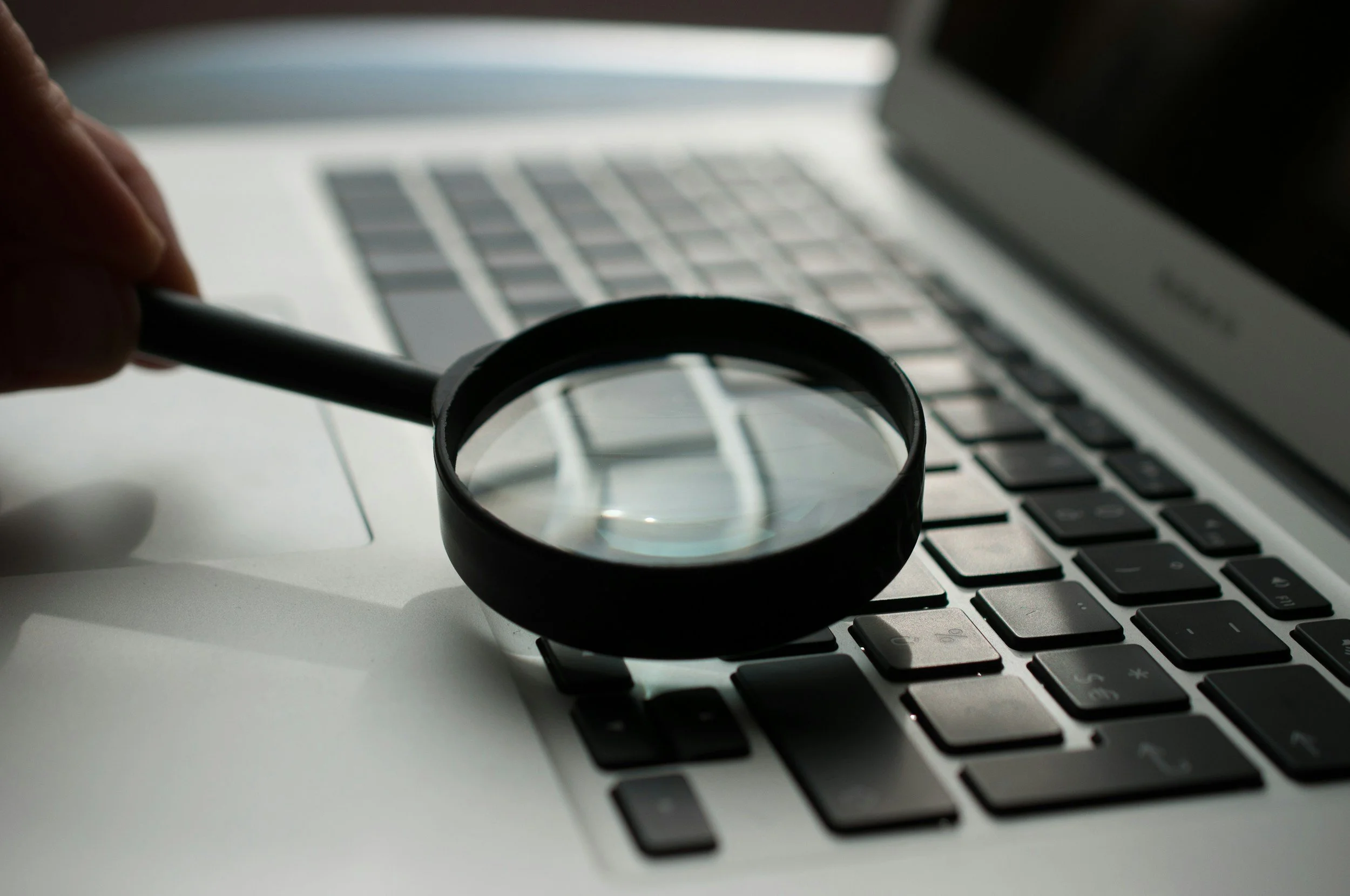 Magnify glass looking at keys on gray laptop computer.