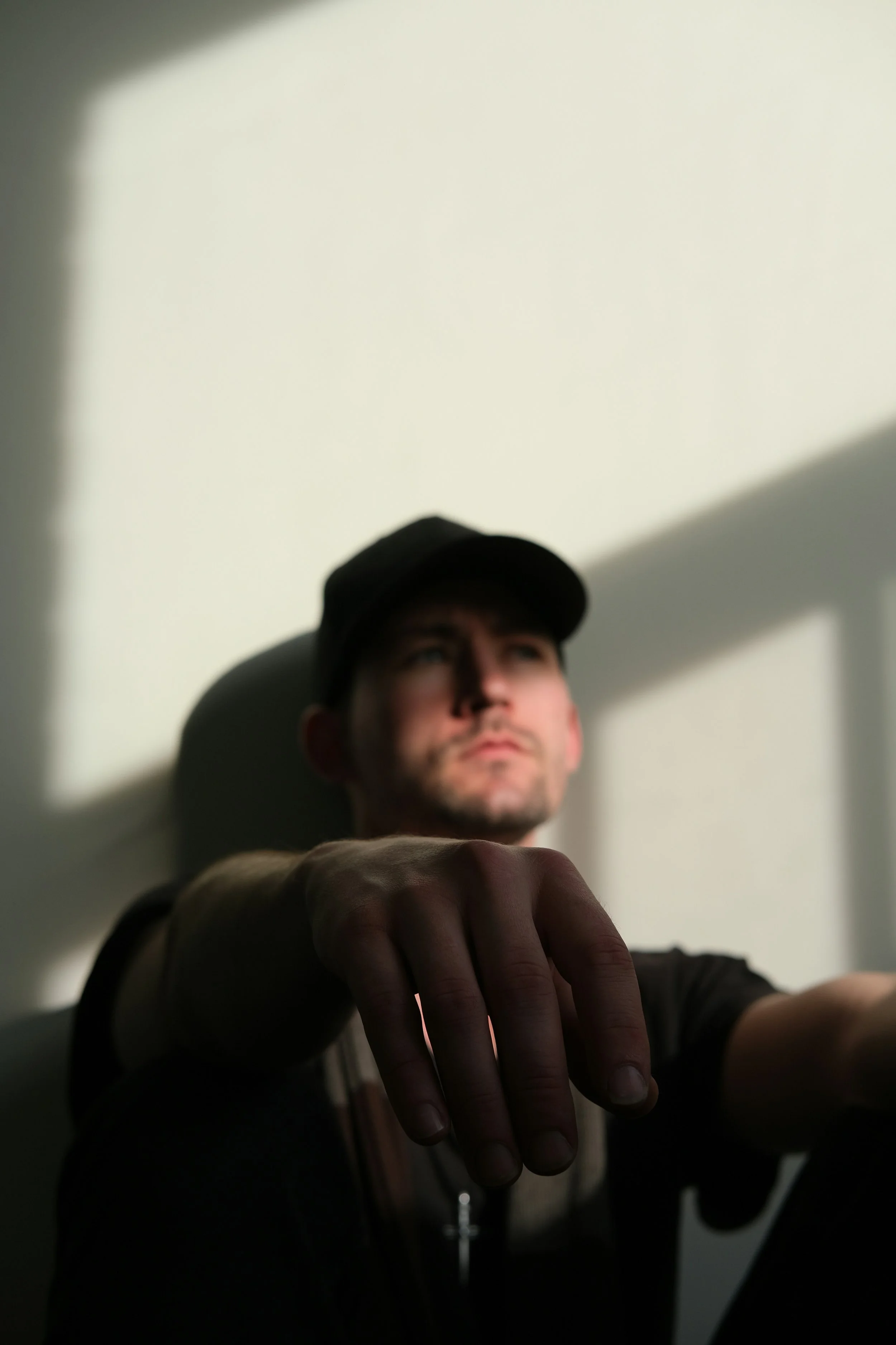 A man sitting against a white wall with the shadows of the window across his face.