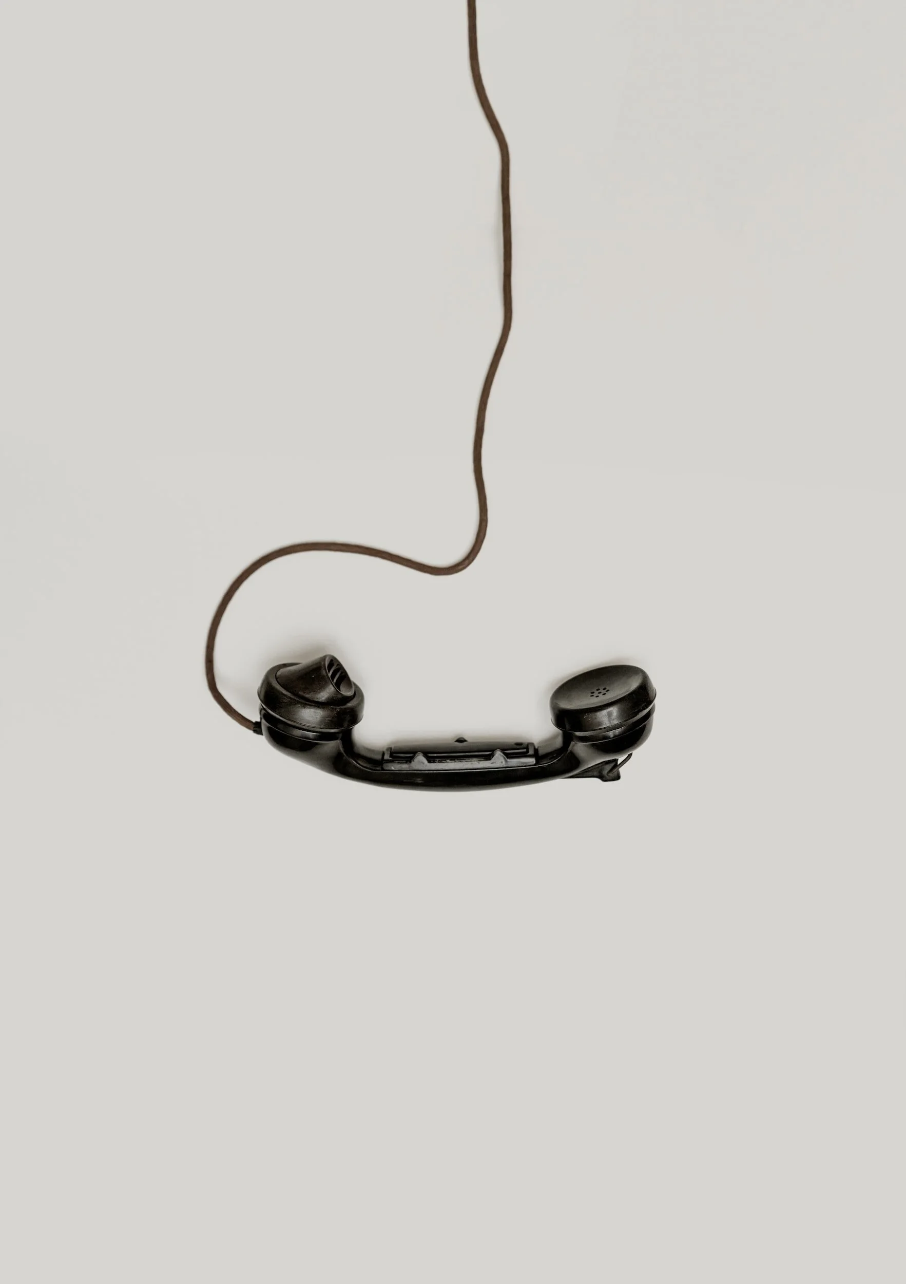 An old black landline telephone handset with a curly cord hanging down, placed on a plain white surface.