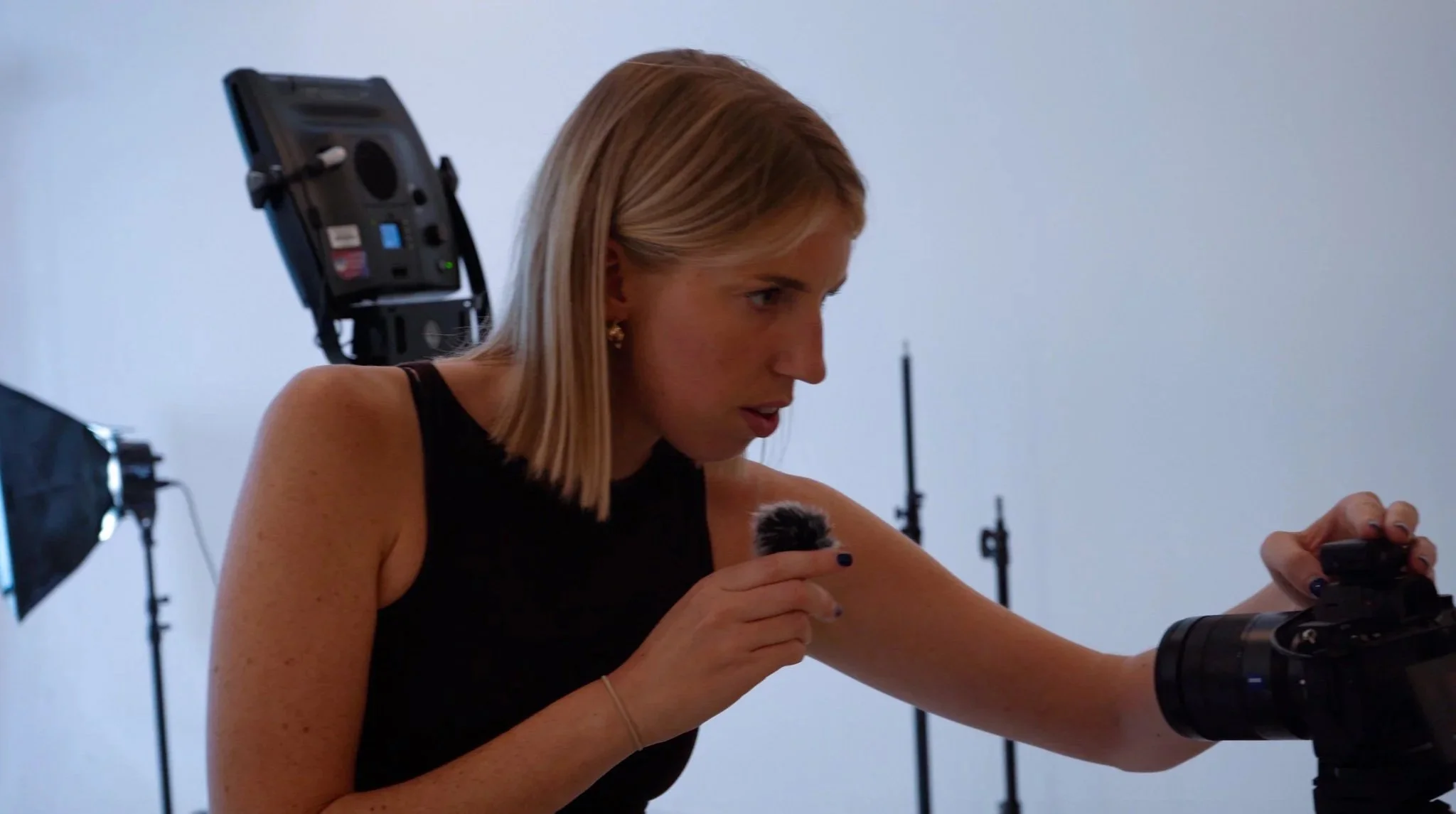 Emily is adjusting camera equipment in a photography studio, surrounded by studio lights and tripods.