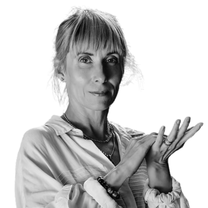 A black and white portrait of a woman with short hair and bangs, wearing a button-up shirt and jewelry, holding her hands together as if in a gesture of explanation or emphasis.