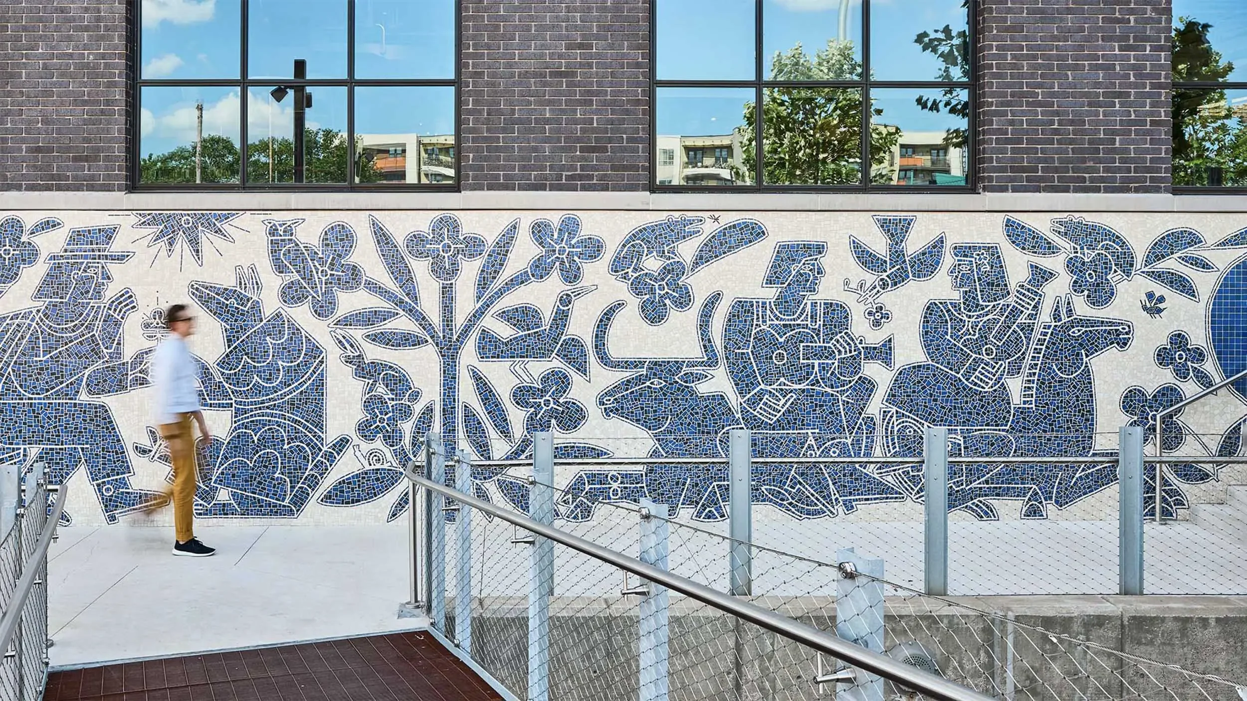 Person walking past America Martin's "Armadillo's Song," showing the monumental scale of the 70-foot hand-cut Otomi mosaic mural at Centro, East Austin, TX.