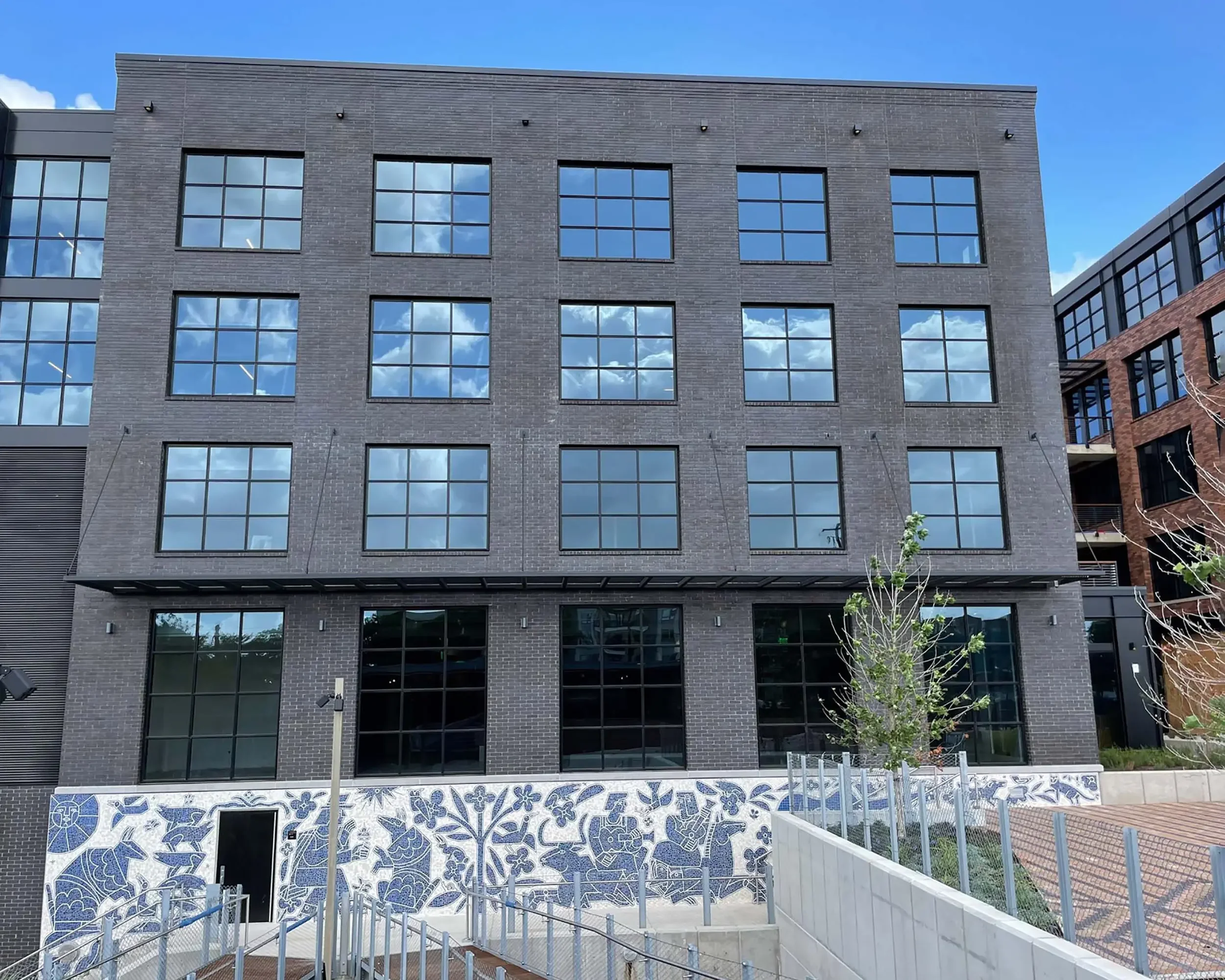 Daytime frontal view of America Martin's "Armadillo's Song" hand-cut Otomi mosaic mural at Centro, East Austin, TX. The Colombian-American artist's 70-foot blue and white public art installation features intricate indigenous figurative motifs across 