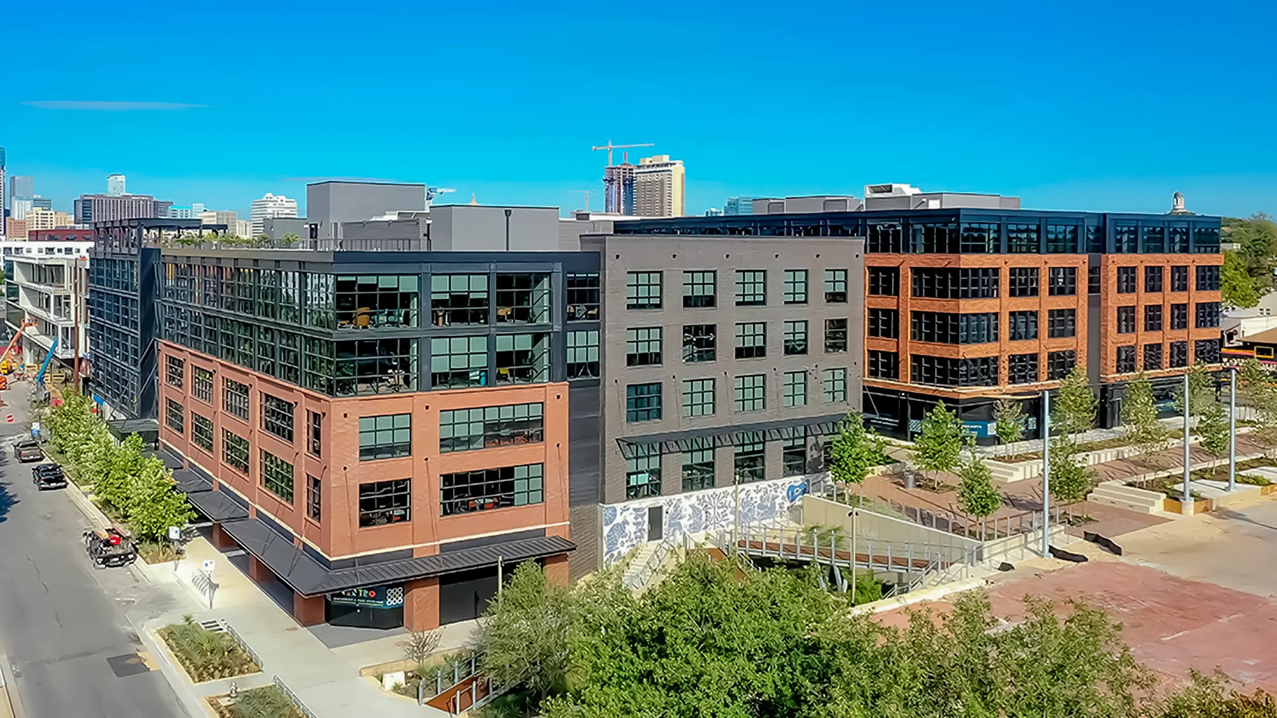 Wide aerial view of Centro mixed-use development in East Austin, TX featuring America Martin's "Armadillo's Song" — a 70-foot hand-cut Otomi mosaic mural in blue and white by the Colombian-American artist, visible on the exterior courtyard wall with 