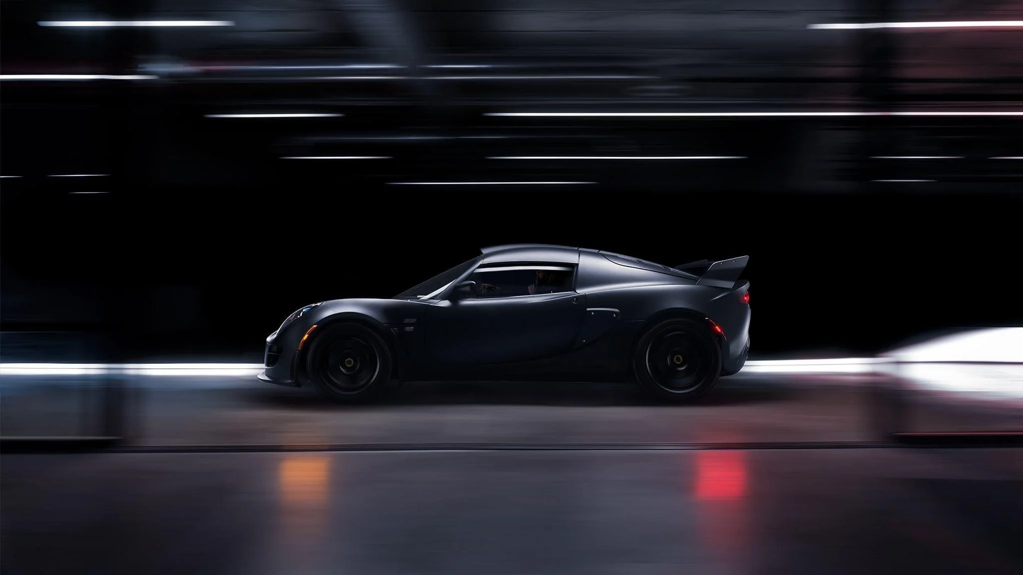 A sleek black sports car driving through a tunnel at night with motion blur.