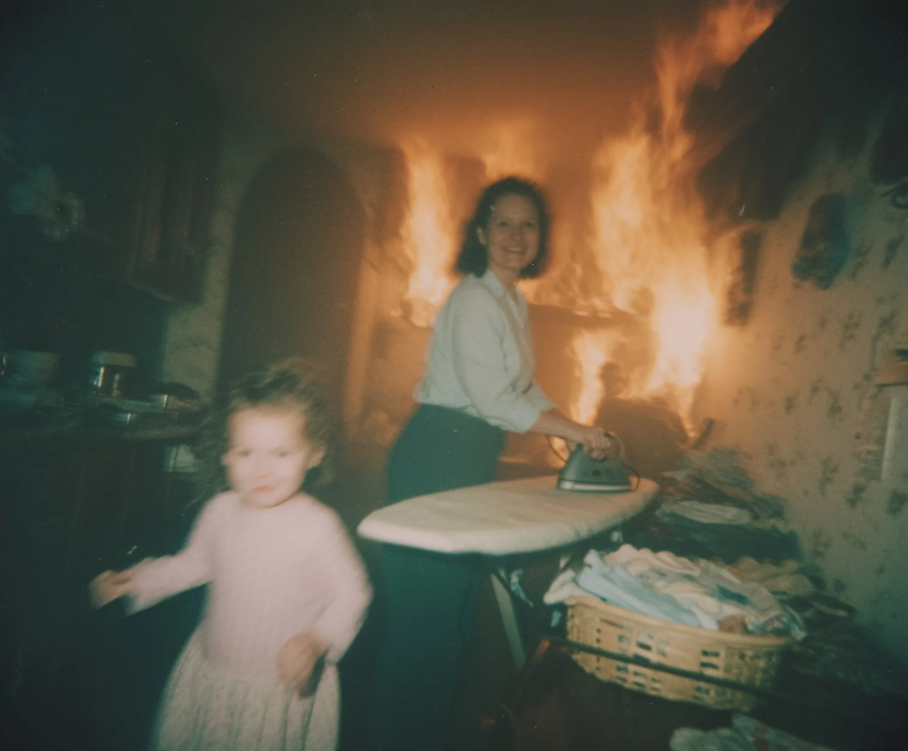An indoor scene with a woman and a child near a fireplace with flames. The woman is smiling and ironing, while the child is standing in front of her, slightly out of focus.