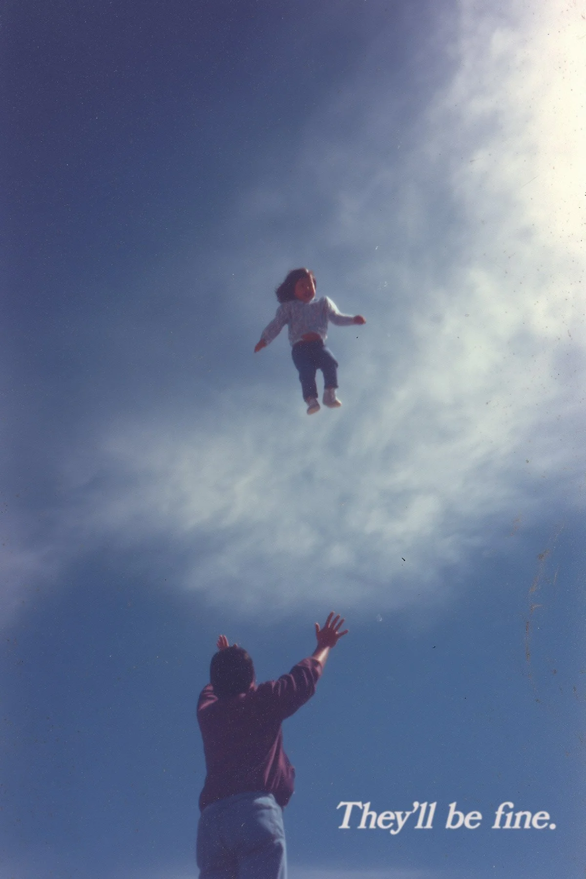 A person in a maroon jacket reaches upward as a girl in a hoodie is flying through the sky with outstretched arms, against a backdrop of a partly cloudy sky with sunlight. Text in the bottom right corner reads, "They'll be fine."