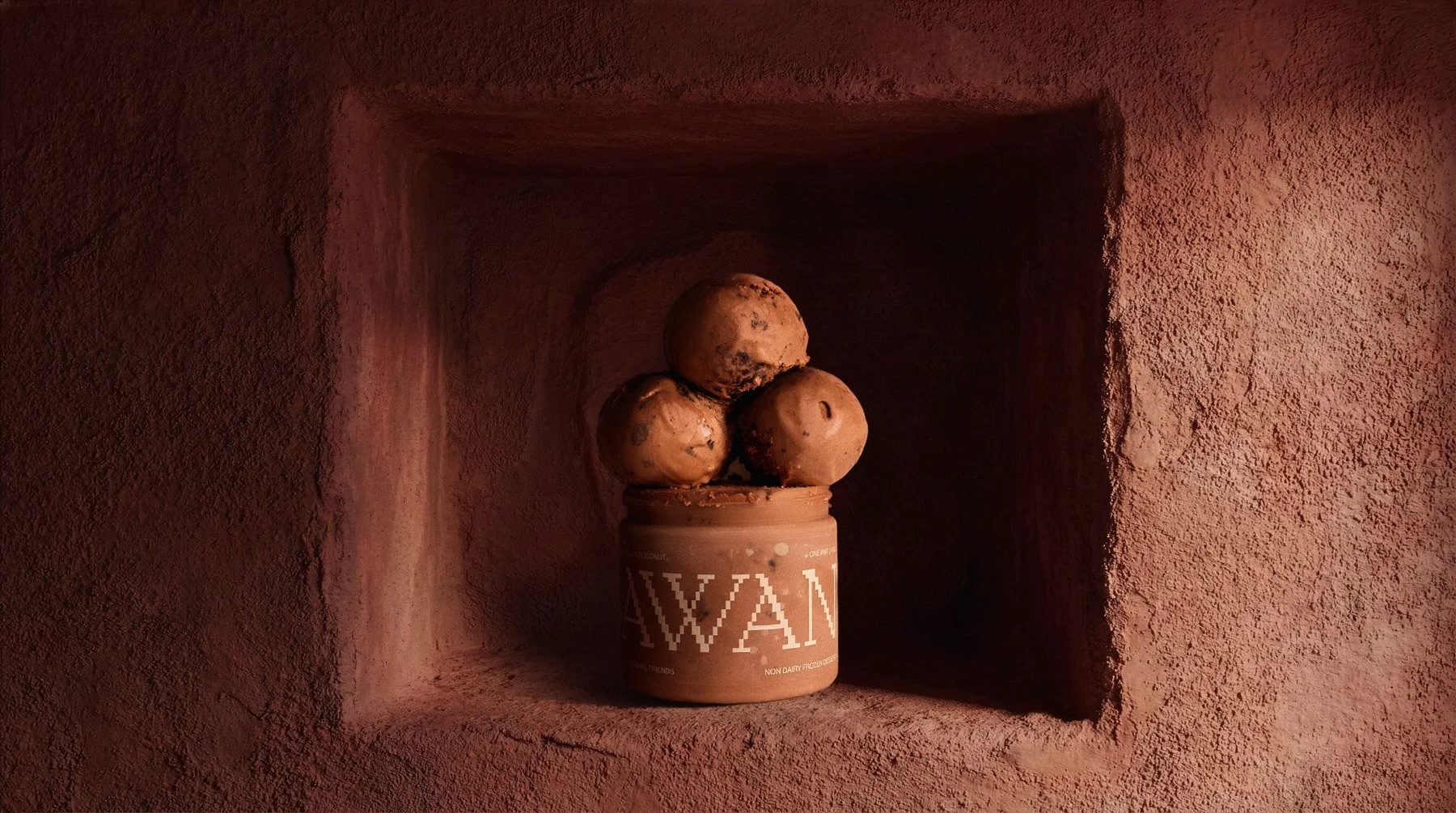 A pint of plant-based ice cream with three large scoops on top, placed inside a pink textured alcove.