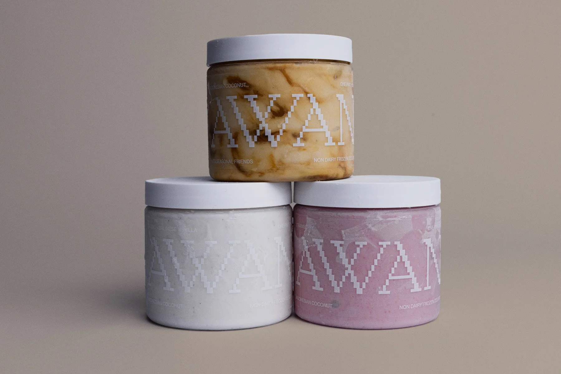Three containers of non-dairy frozen dessert, with the top container in a caramel flavor, and the bottom containers in vanilla and strawberry flavors, all featuring a minimalist design with white lids and brand logo.