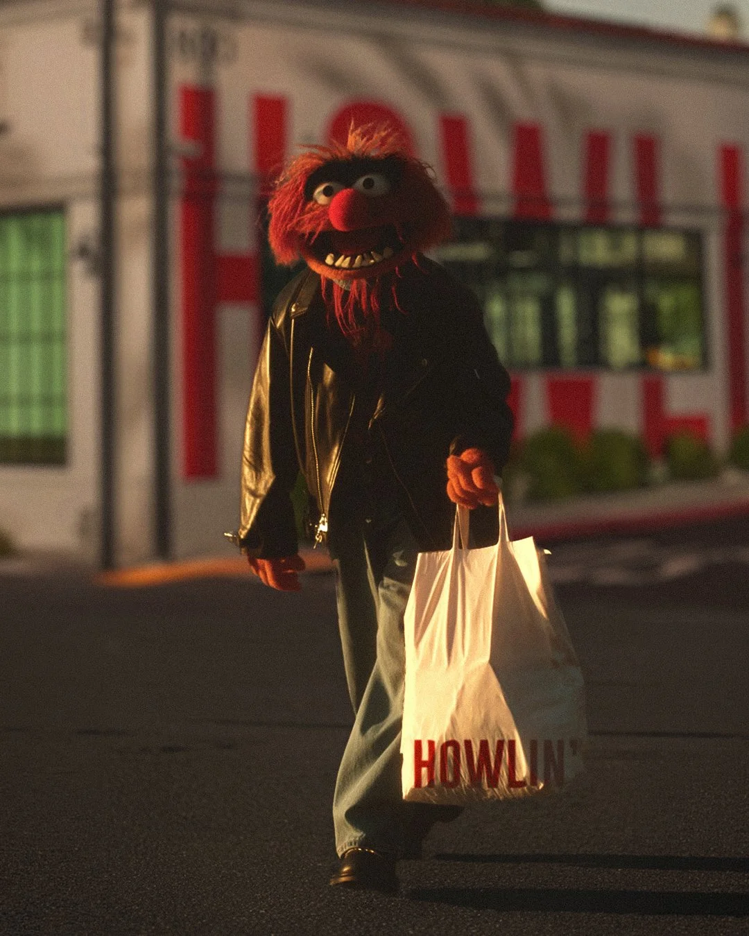 The muppet Animal dressed in a black leather jacket and grey pants, walking in a parking lot at Howlin Rays with a take out bag 