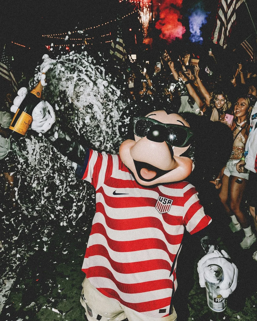 Mickey Mouse wearing a USA soccer jersey at a lively party, holding a bottle of champagne, with foam splashing and people celebrating in the background.