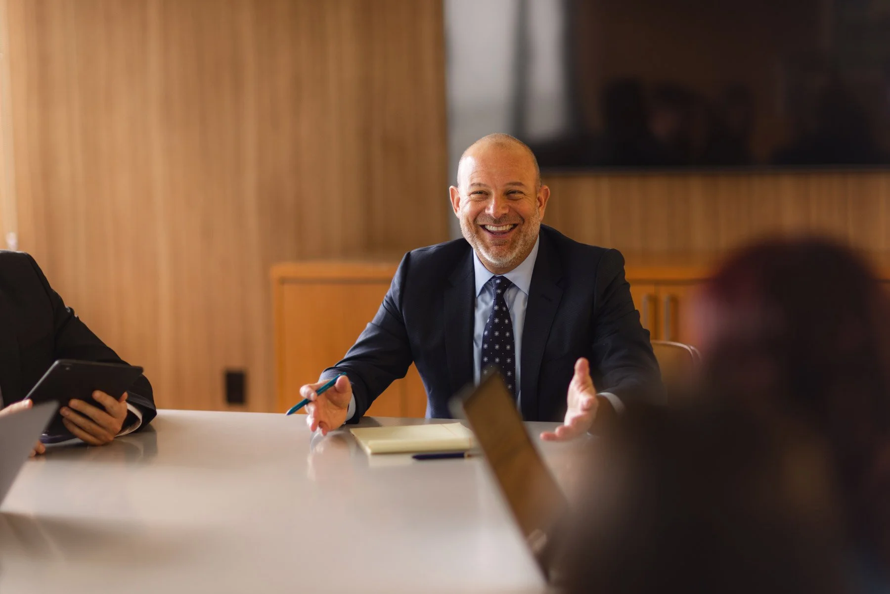 Man in a suit speaking and smiling during a business meeting in a conference room.